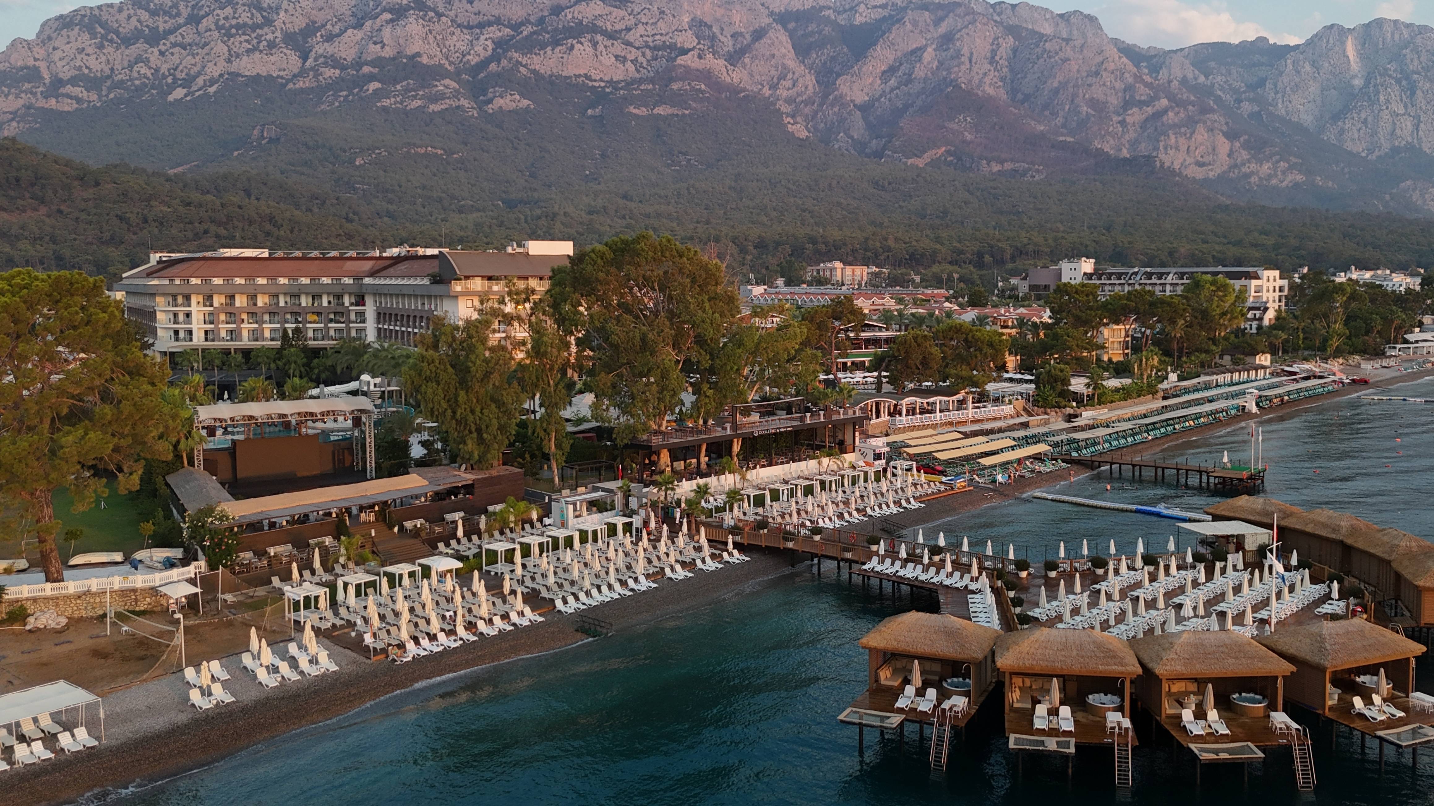 نمای هوایی DoubleTree by Hilton Antalya-Kemer All-Inclusive Resort با ساحل خصوصی، اسکله‌ها، ساختمان اصلی و کوه‌های توروس