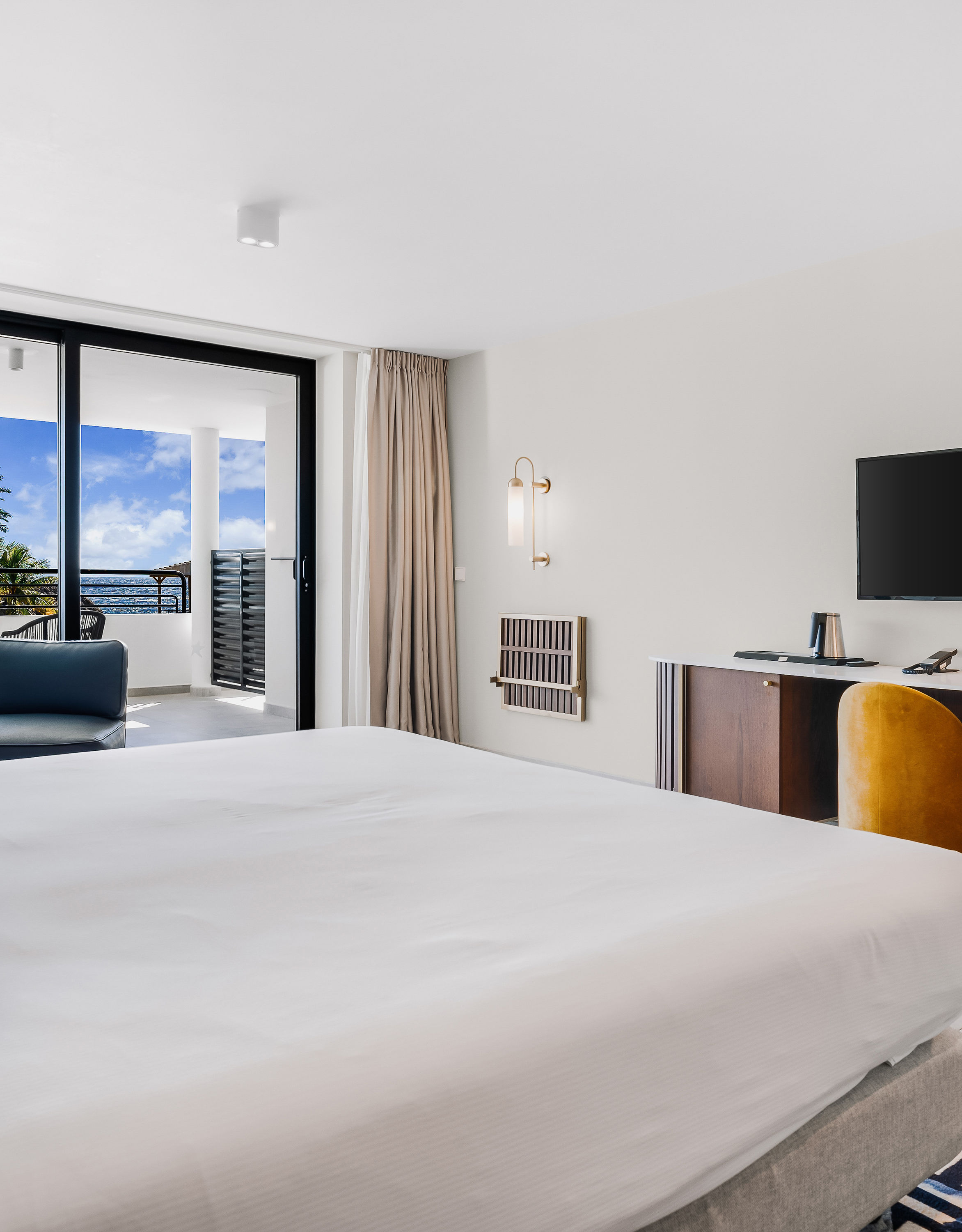 Vista da cama king-size com TV, cadeiras laranja e vista para fora da área da varanda
