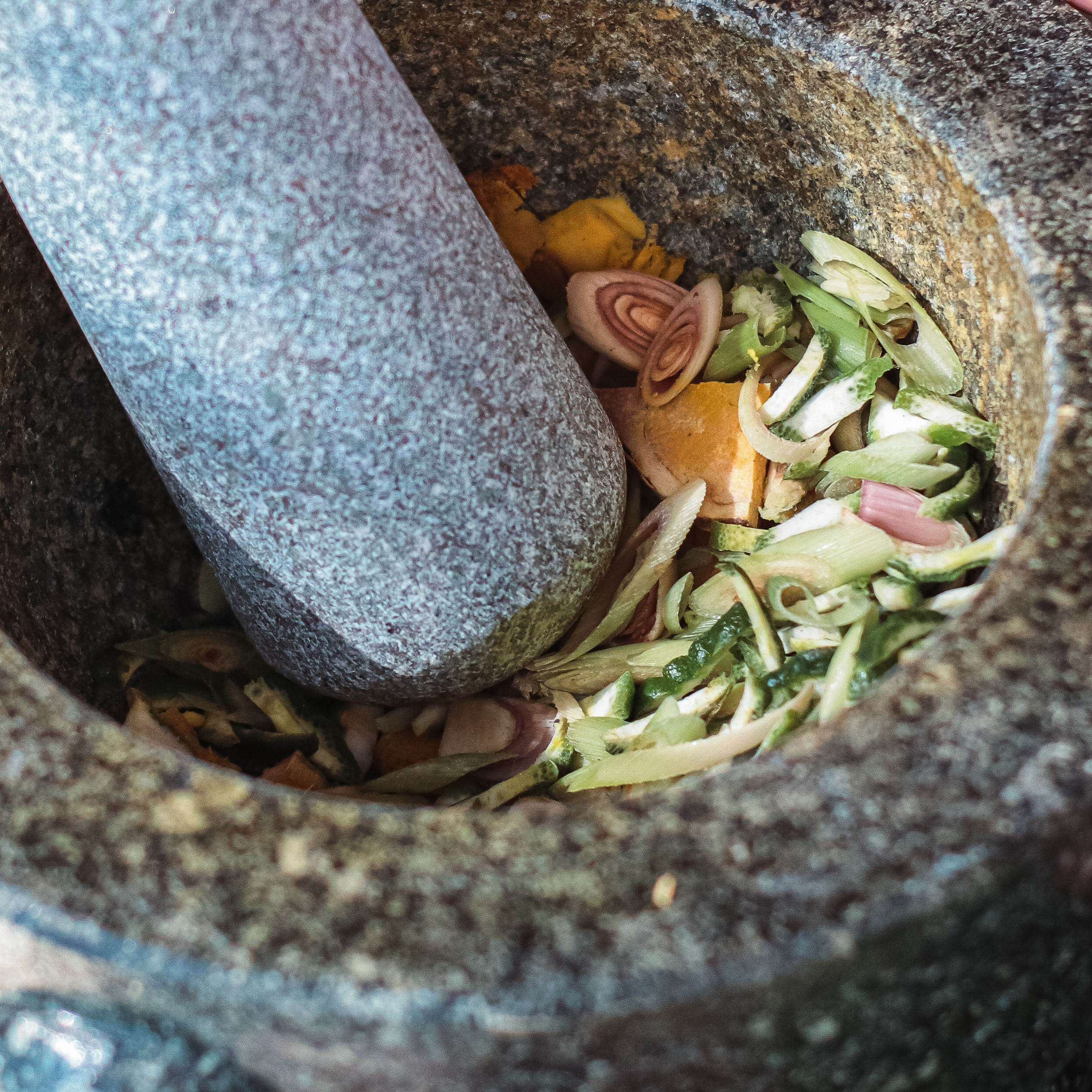 Eine Person, die einen Steinmörtel und Pestle verwendet, zerdrückt frische Kräuter und Wurzeln.