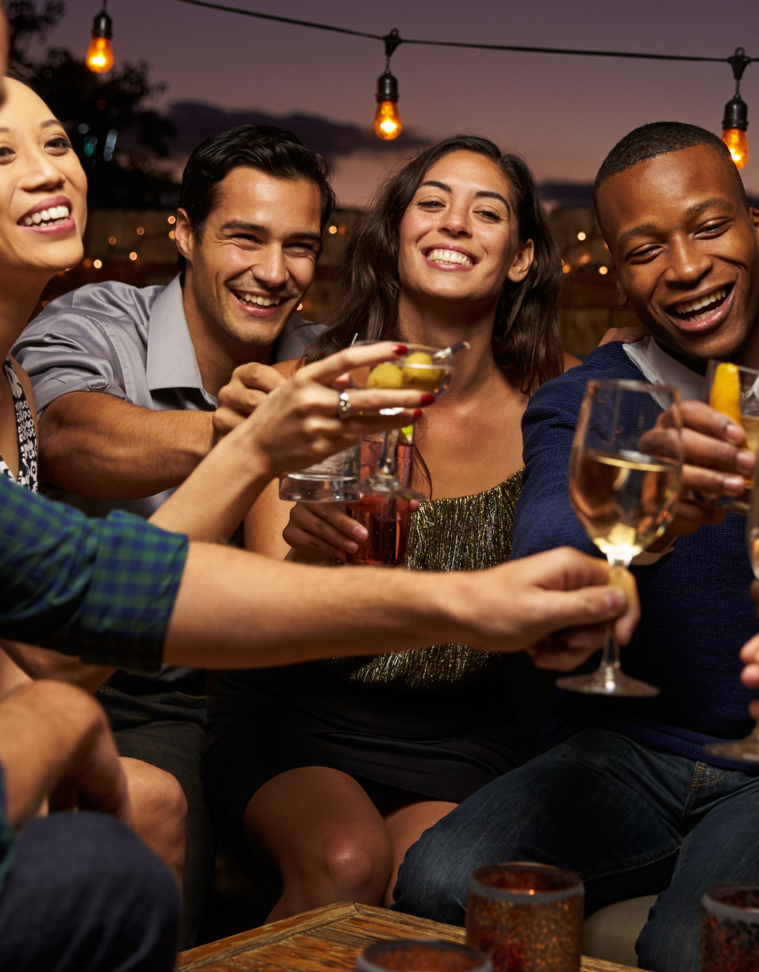 Group of eight young men and women celebrating with drinks  seated outside in a bar at night time