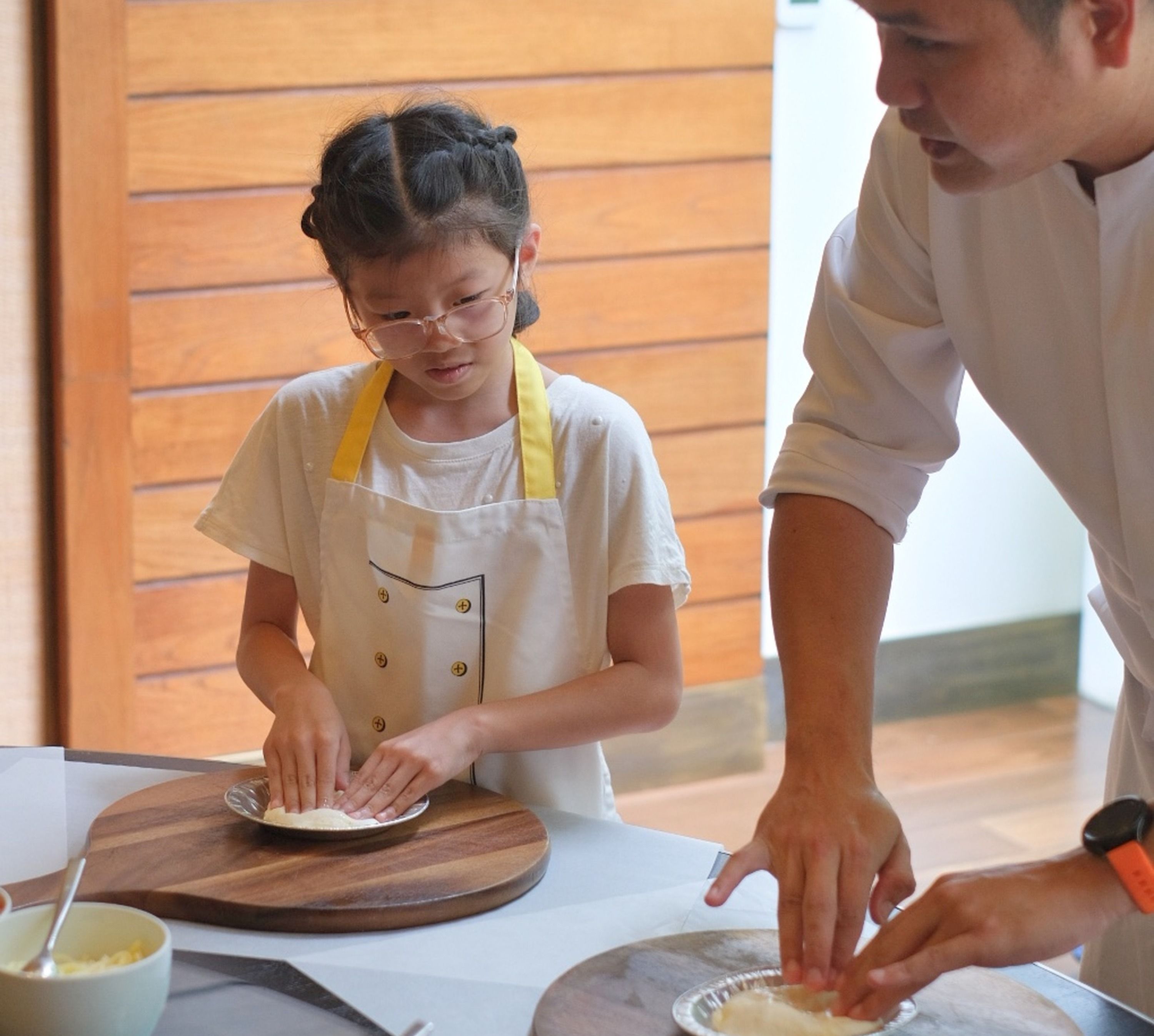 エプロンに身を包んでシェフとピザ生地を作る少女