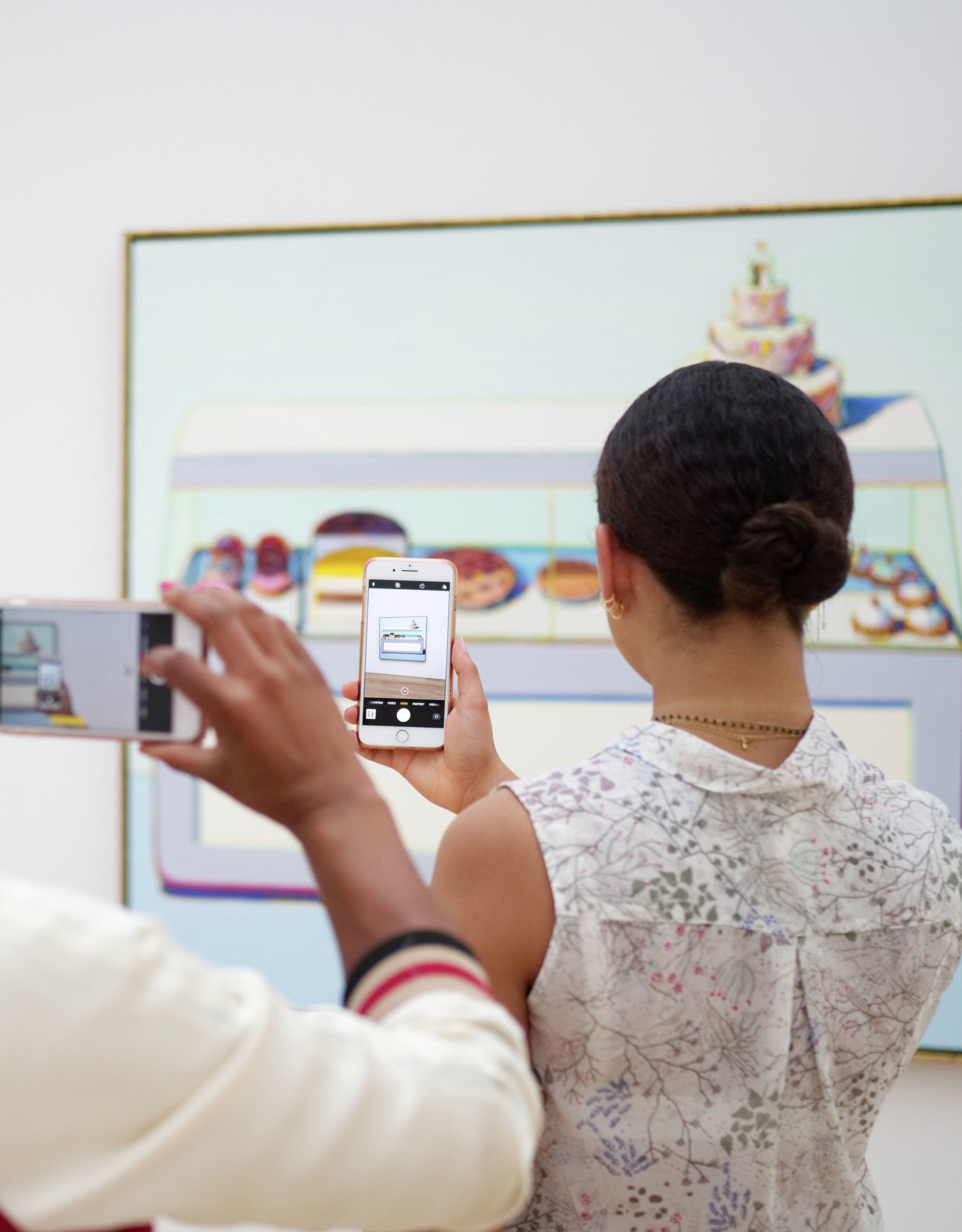 Two women taking photos on phones of art on a wall