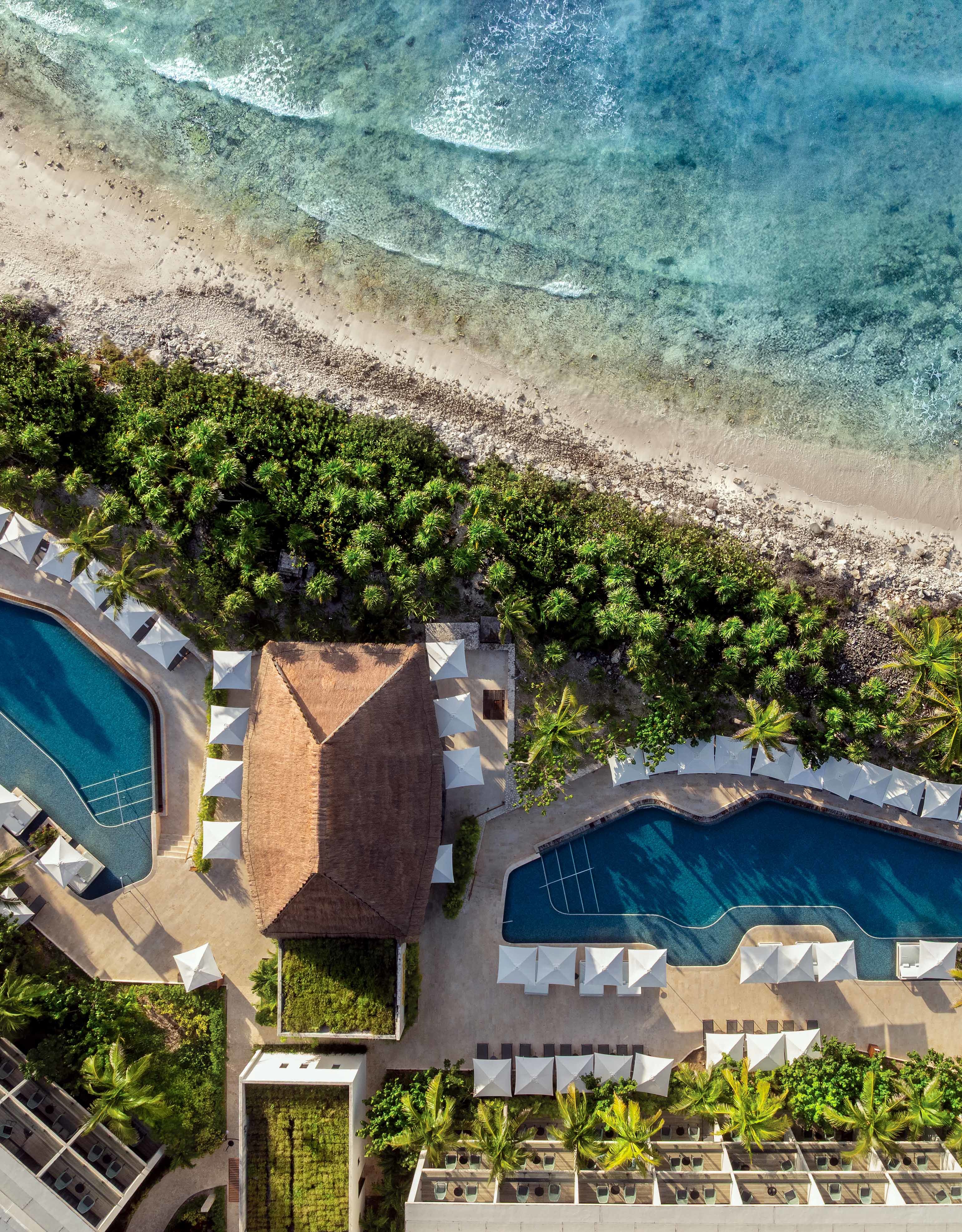 arial view of the beach, 2 outdoor pools, umbrellas, trees and tiki hut