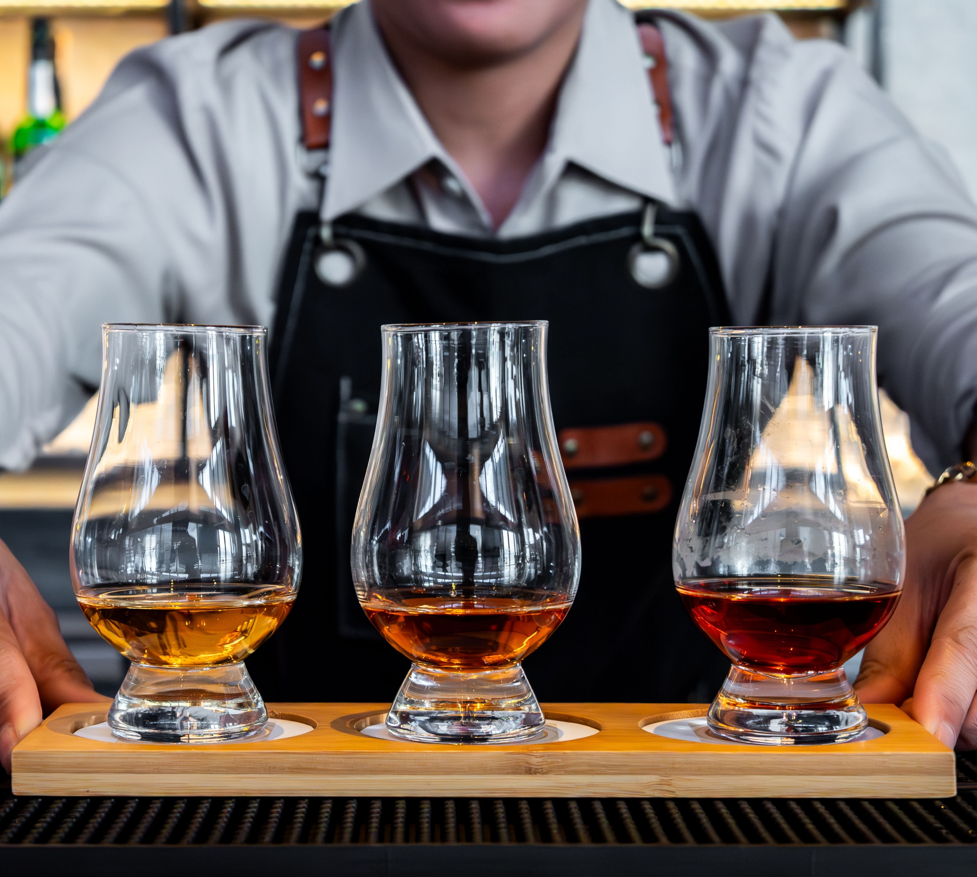 Barman die een dienblad vasthoudt met drie glazen whisky in de C Lounge