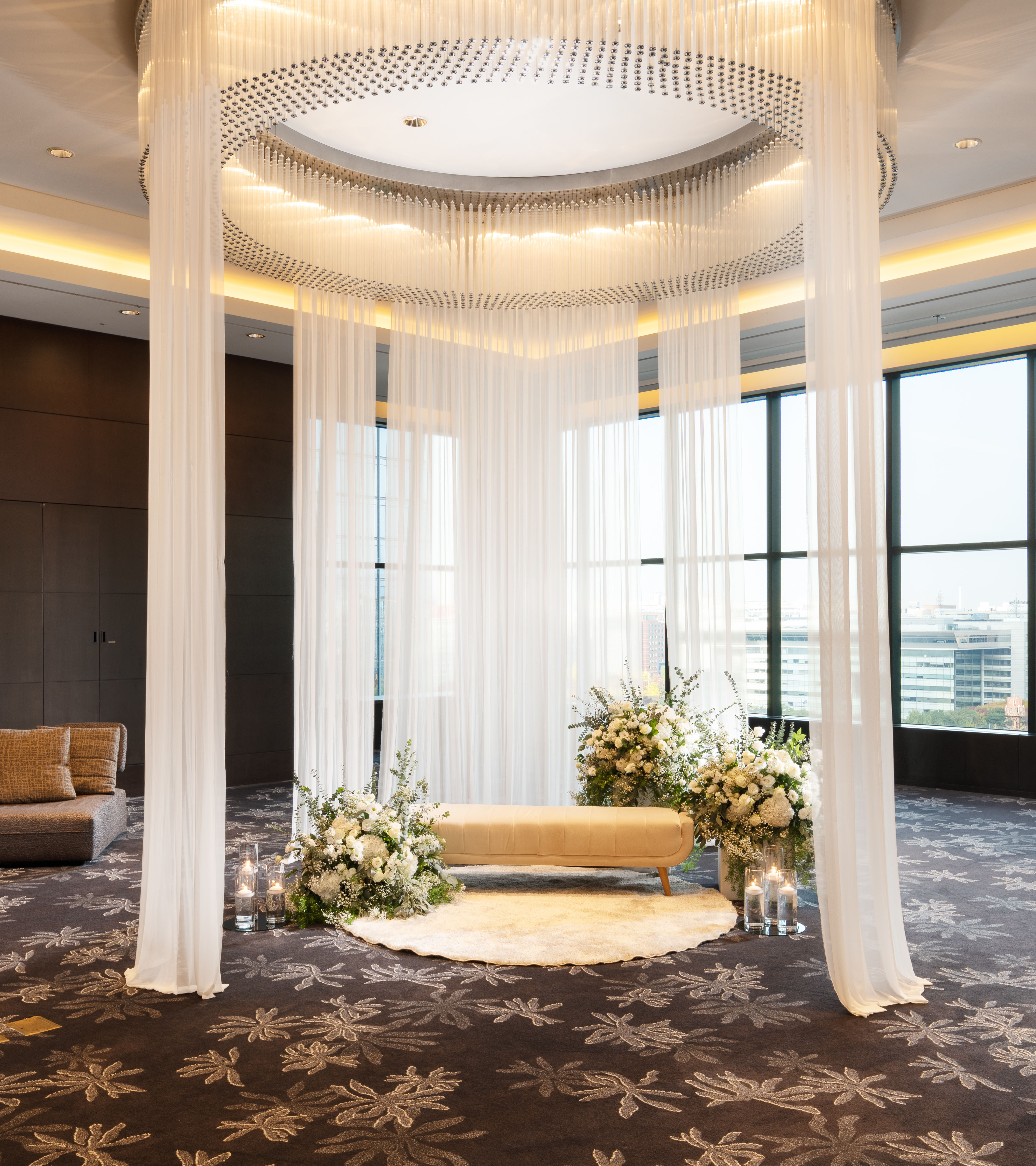 Bridal suite. Floor to ceiling windows light the beautifully decorated room. Sheer curtains and flowers surround a lounge couch in the center of the room.