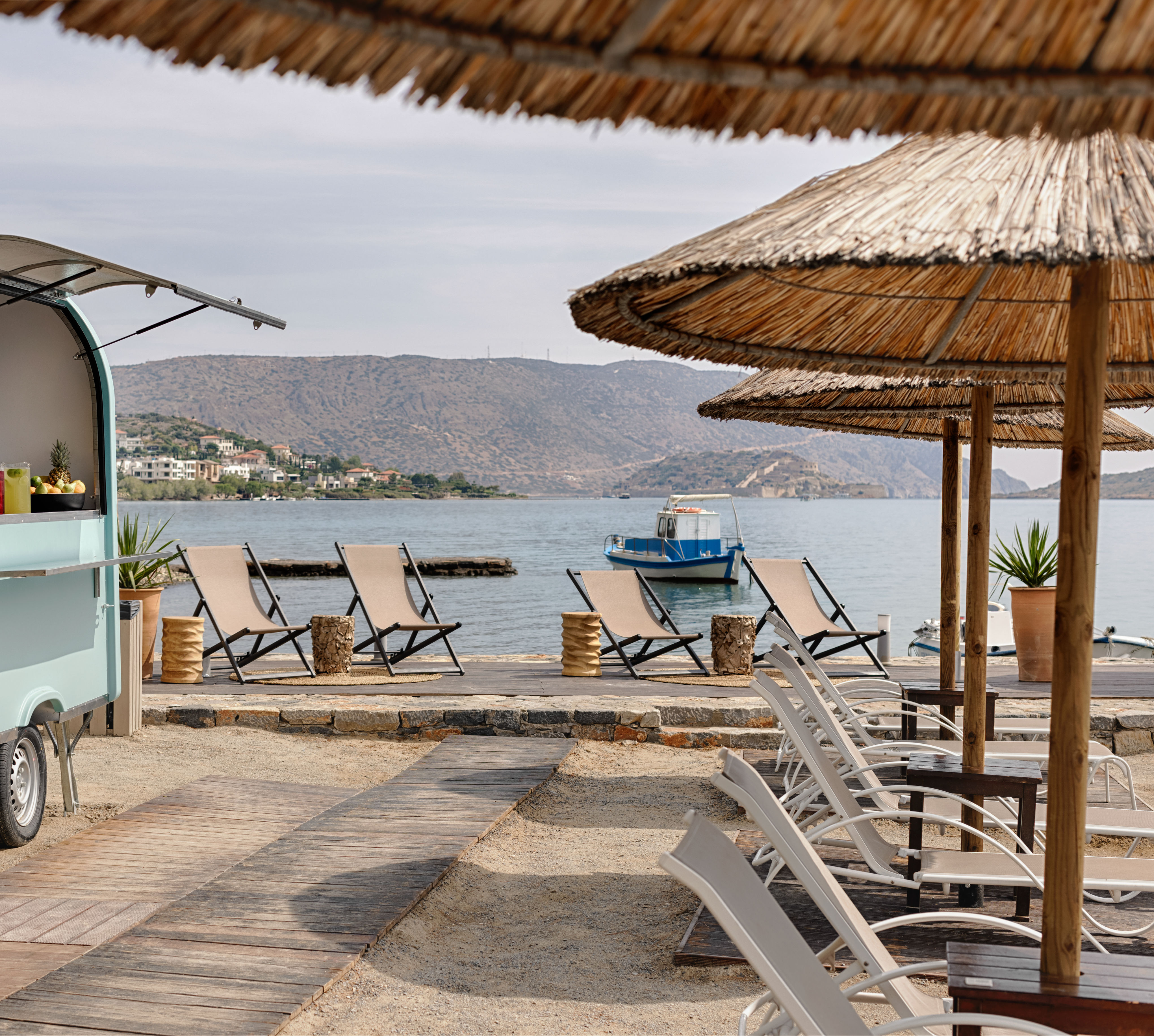 Ammos Beach Bar with straw umbrellas, reclining chairs, a light blue food cart.