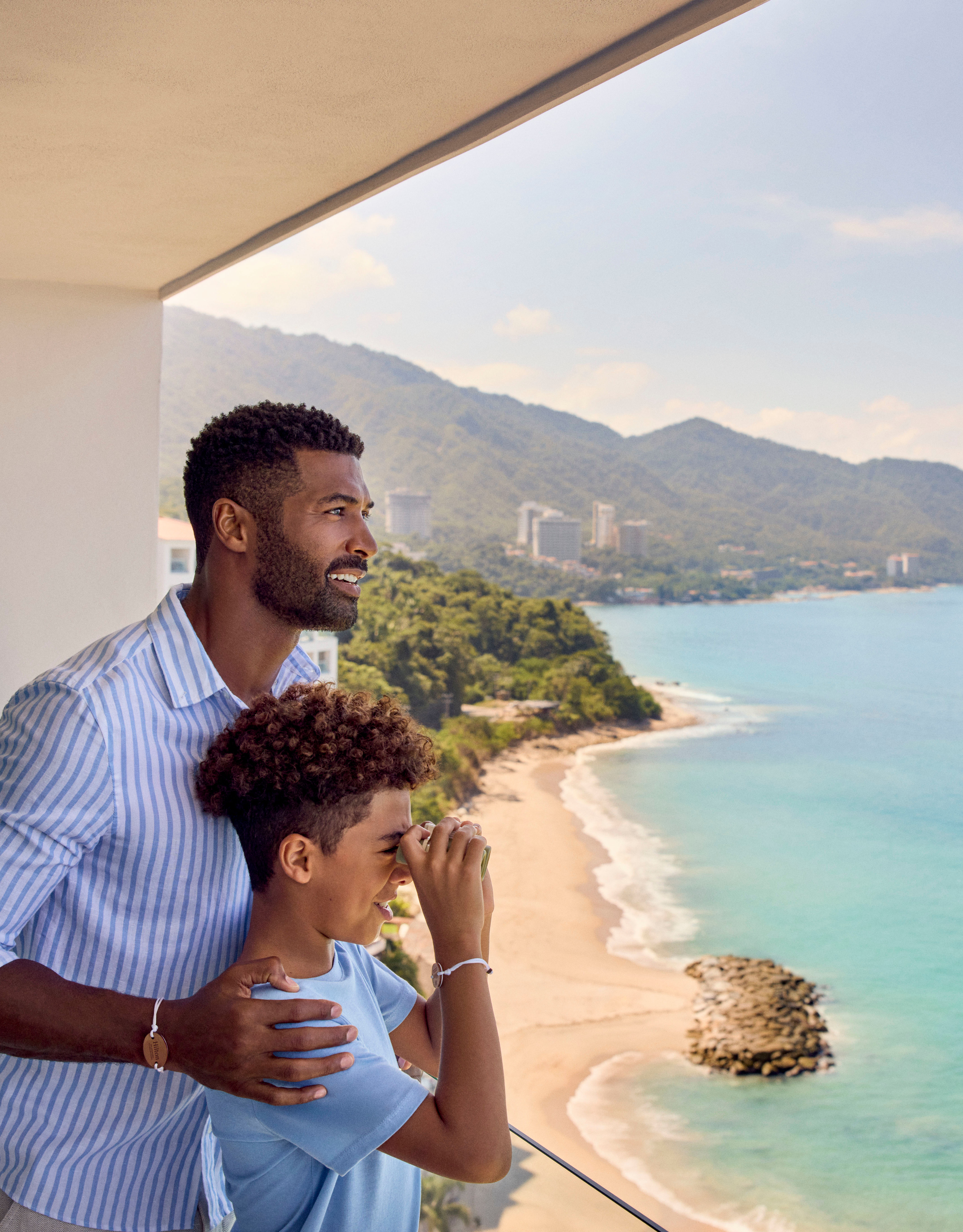 Père et fils debout sur le balcon d'une suite donnant sur la mer avec des jumelles
