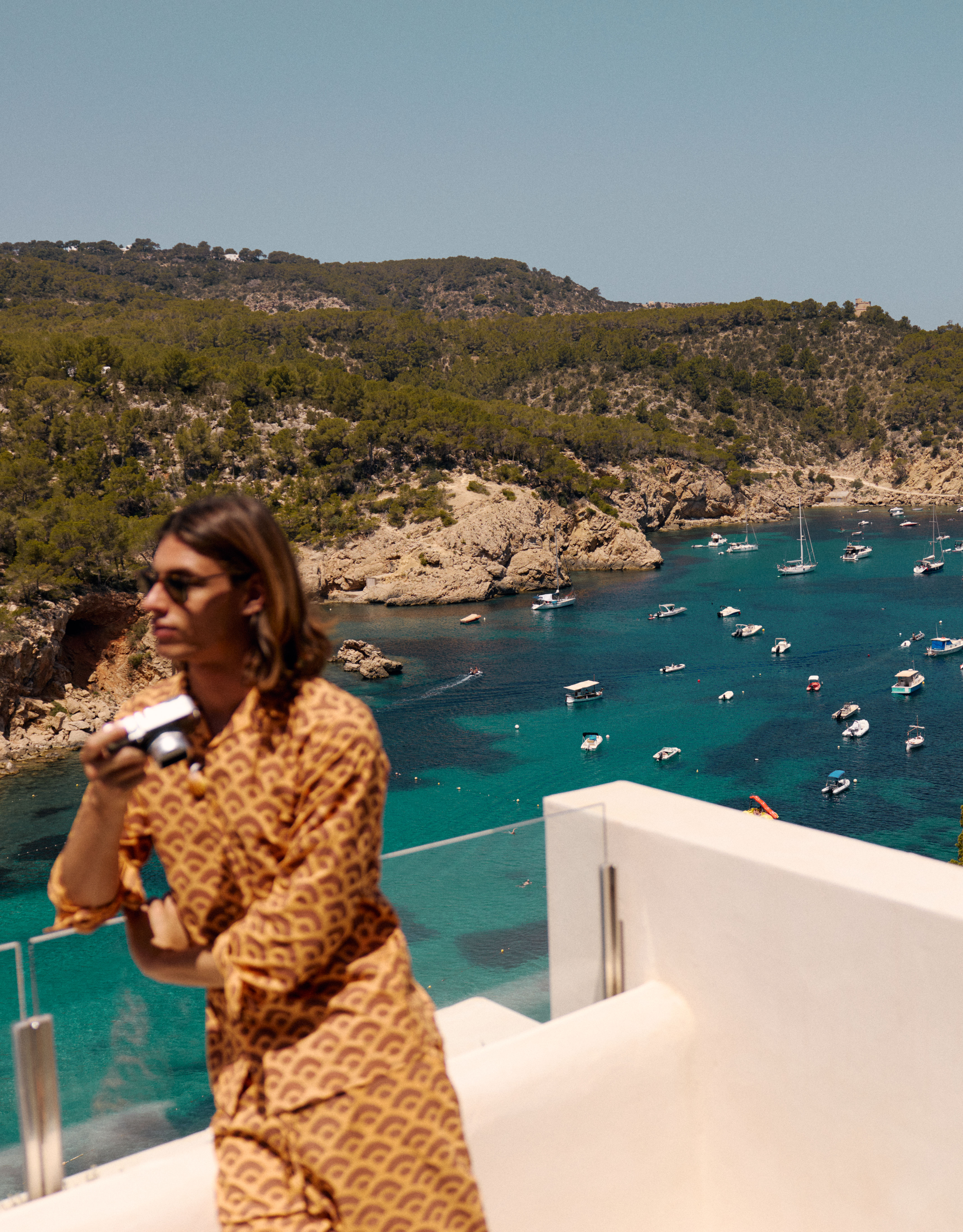 Person, die auf dem Balkon steht und eine Kamera mit Blick auf die Bucht und die Boote hält