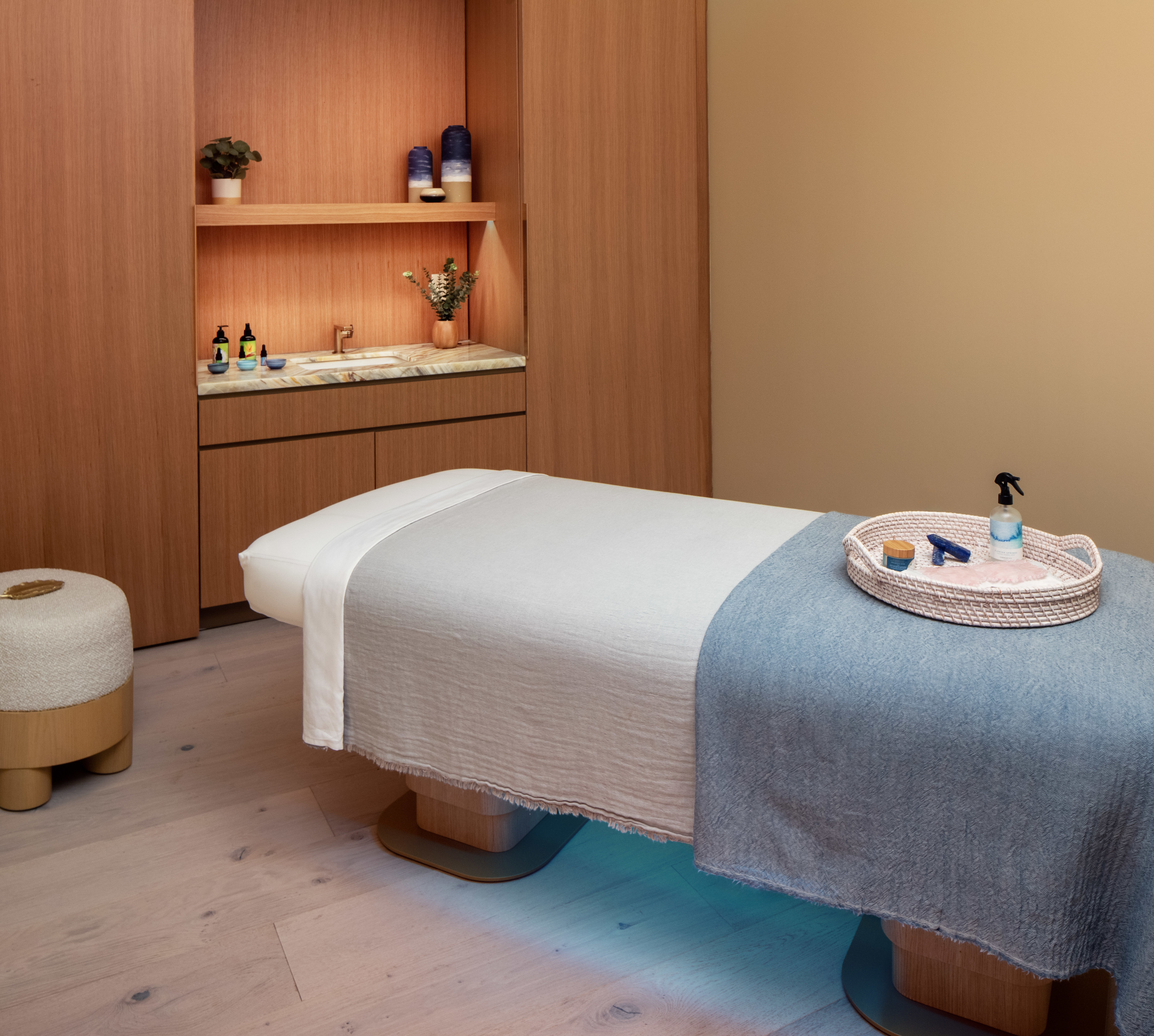 The spa treatment room with
  massage table, mood lighting, and products sitting in a weaved tray.