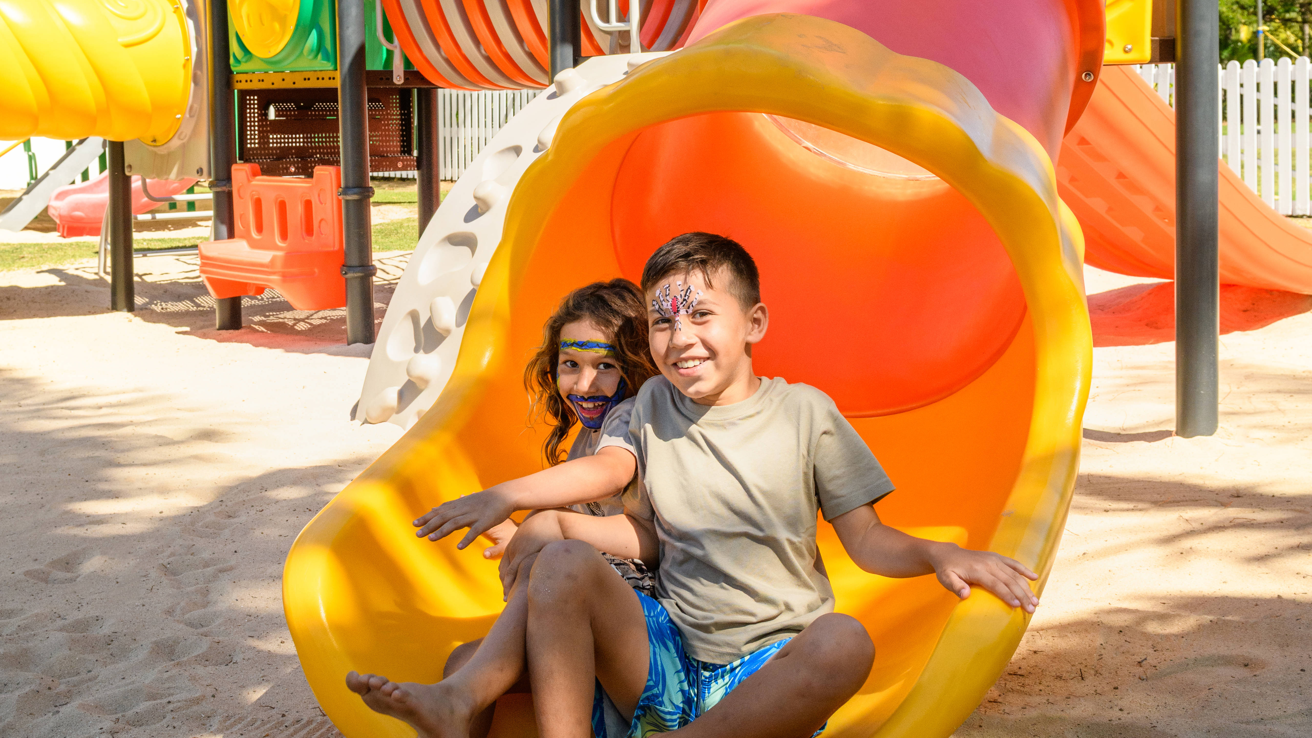 Chlapec a dívka sedí na jedné ze skluzavek v dětském klubu.