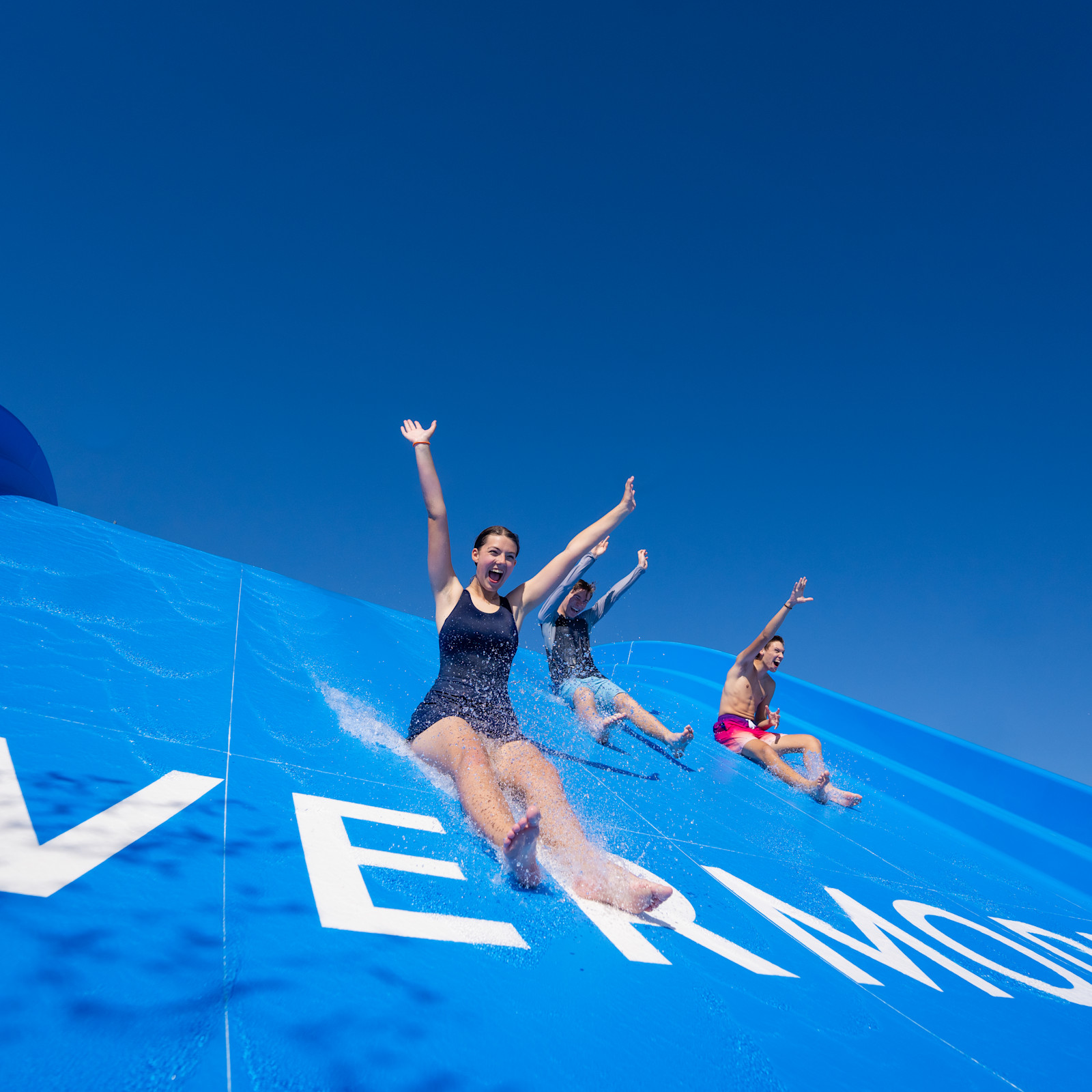 Three people laughing with arms outstretched as they descend water slide