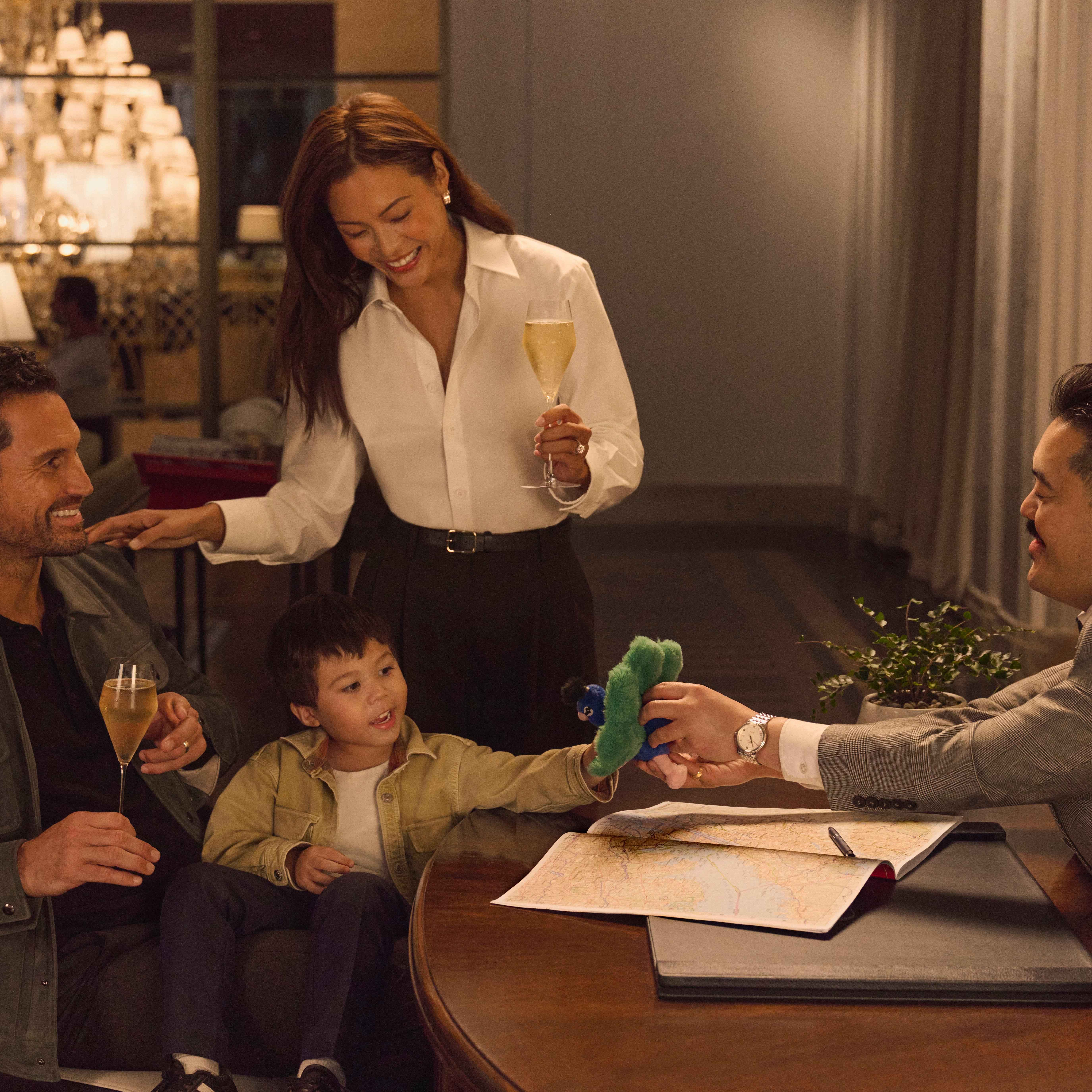 Une mère et son père dégustent un verre de vin mousseux assis au concierge et reçoivent les recommandations du concierge. Le concierge surprend son jeune fils avec un jouet doux au paon.