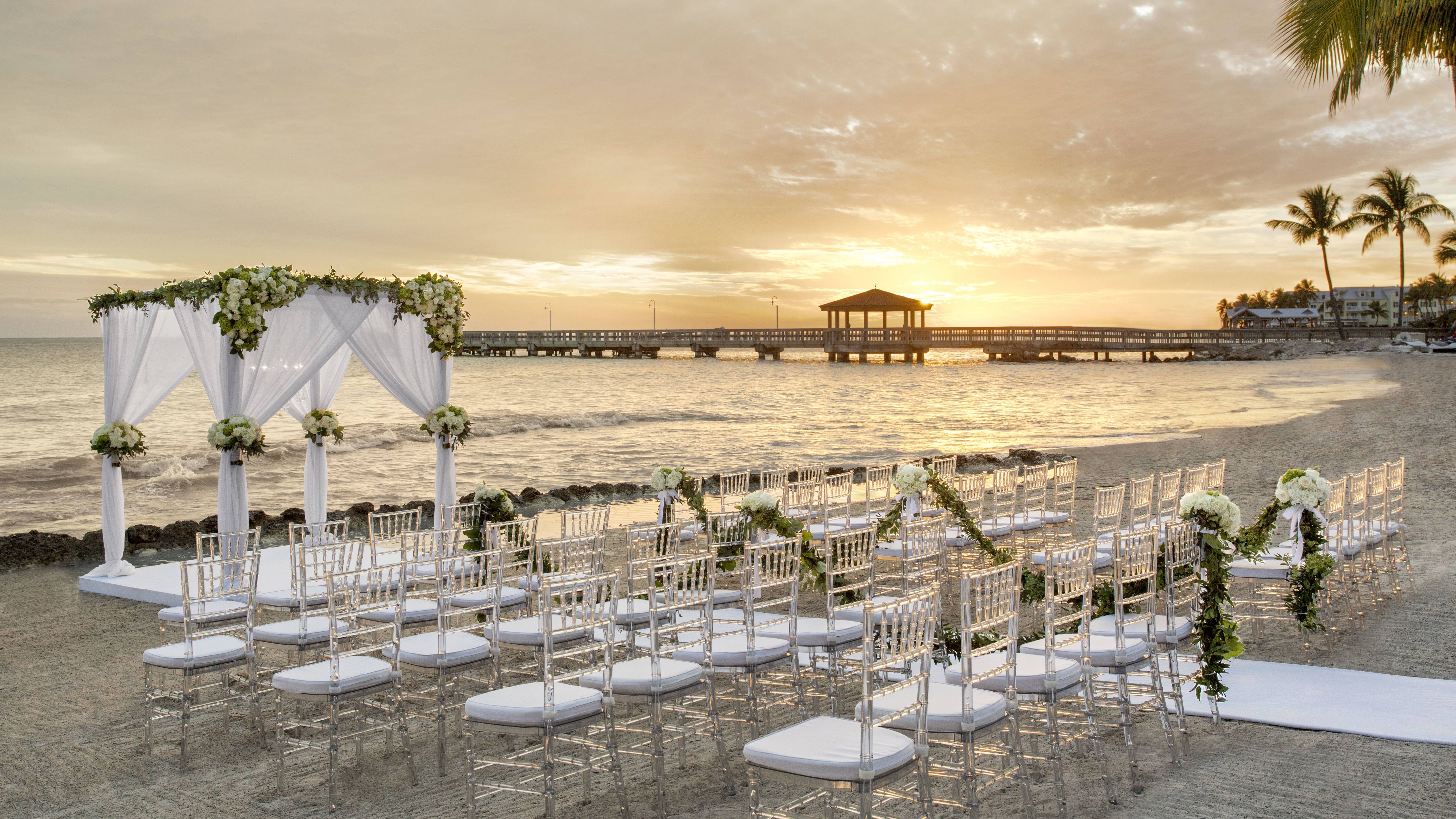 beach wedding ceremony set up, white chairs, gazebo, at sunset
