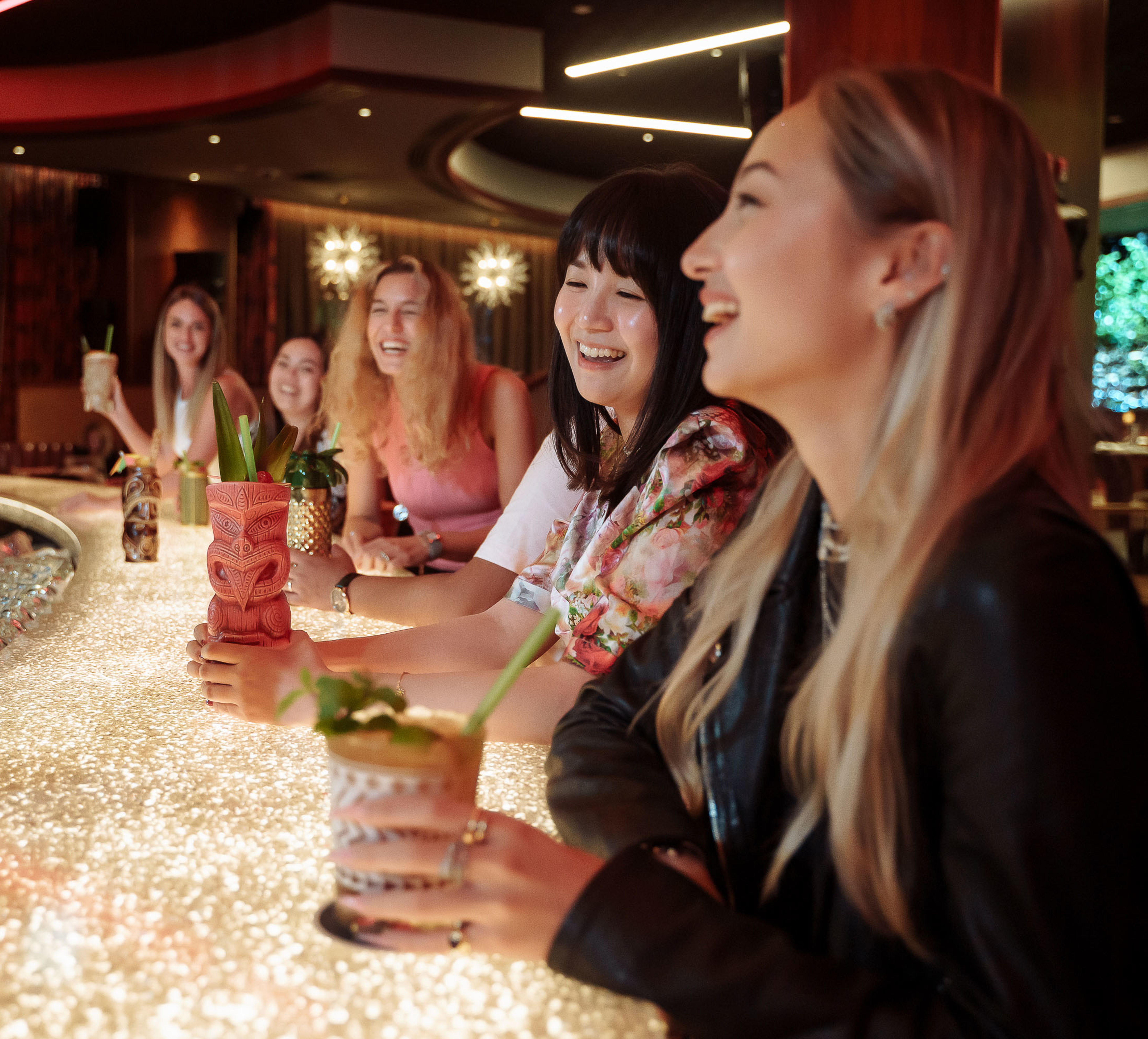 Five women smiling whilst sitting at bar with drinks