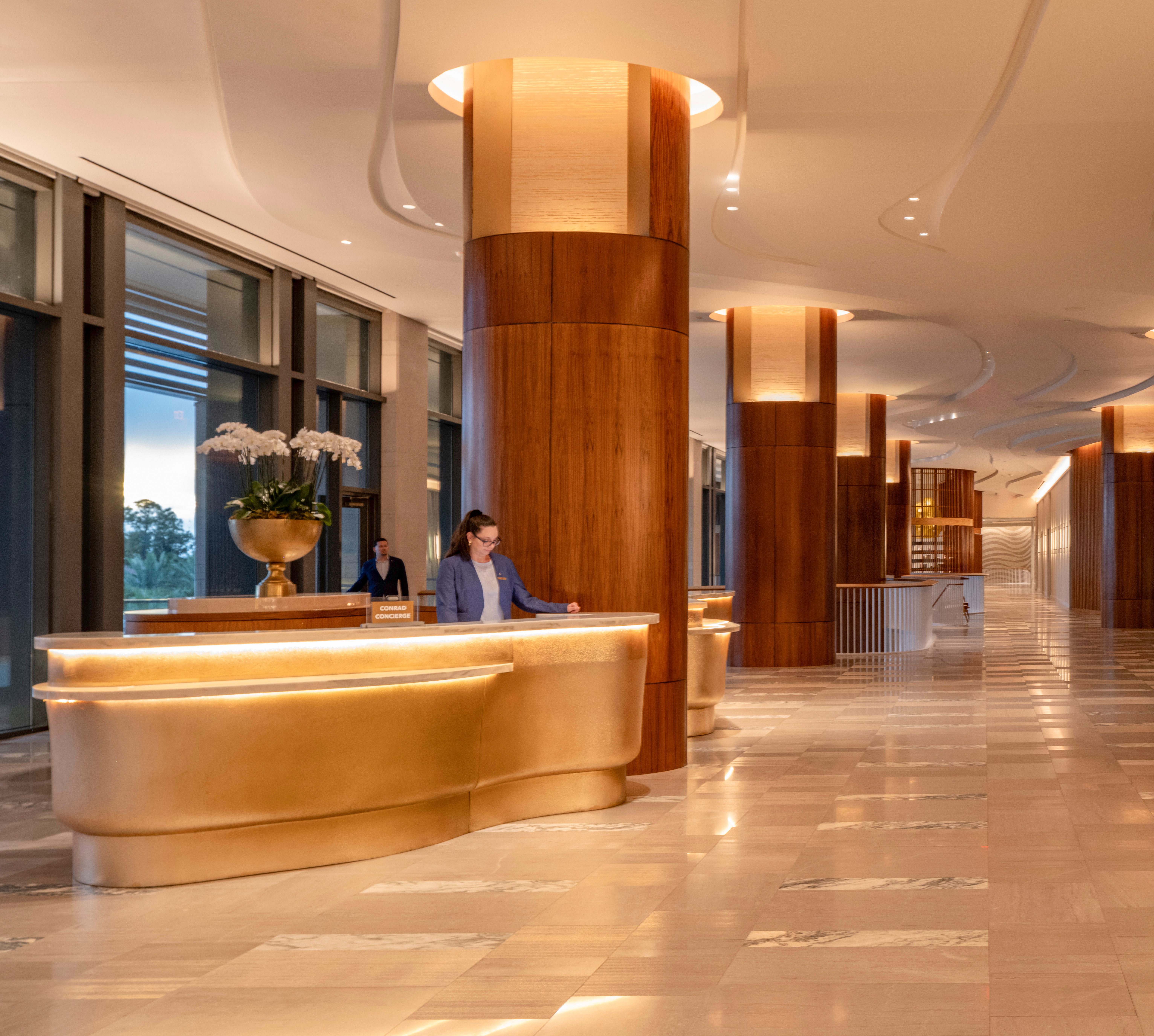 Team Members at the Reception Desk, and a Woman Walking in Lobby Area