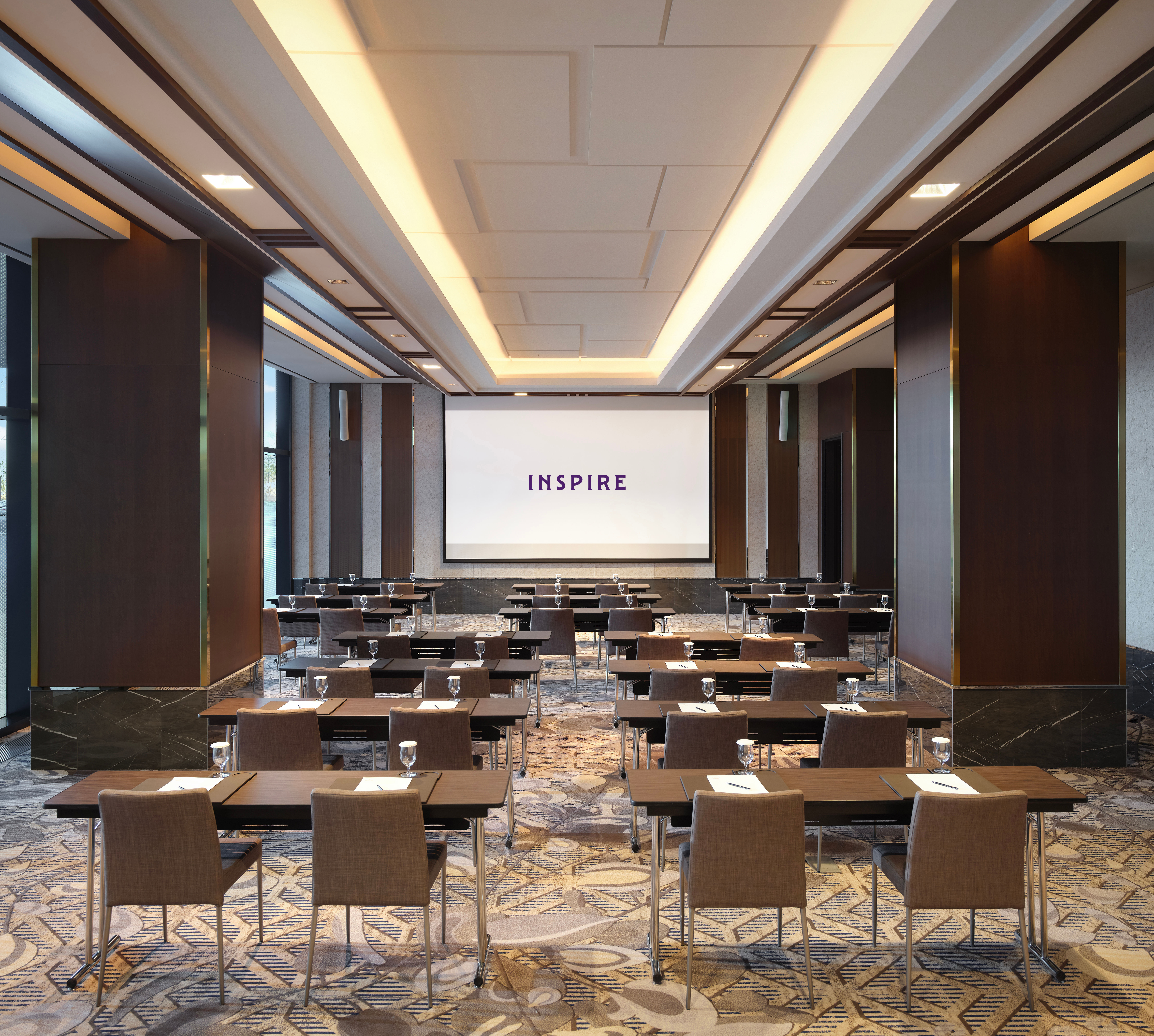 Ruang pertemuan dengan meja, kursi, dan proyektor yang menampilkan logo properti