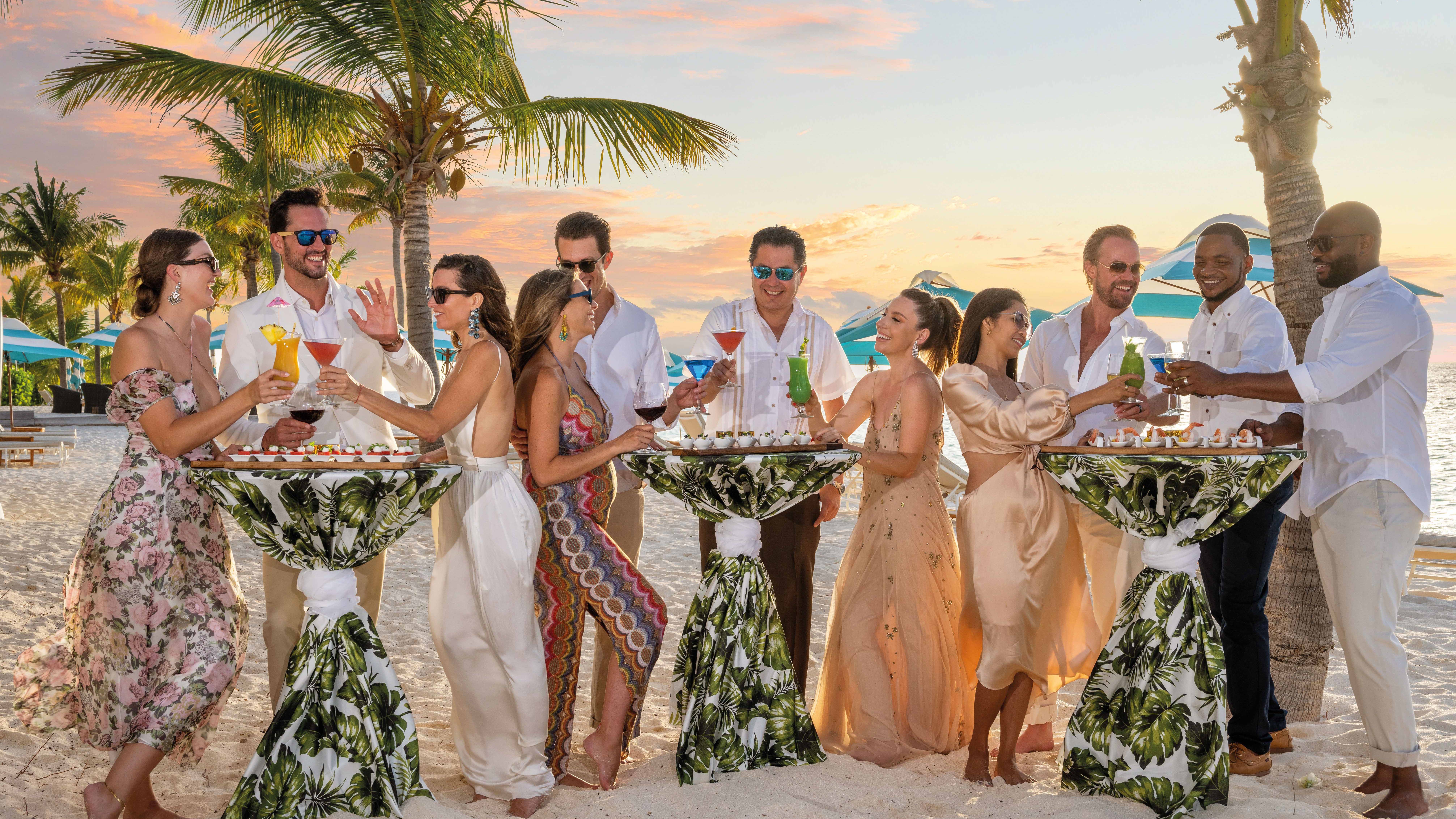 Wedding guests standing at plinths on beach with cocktails