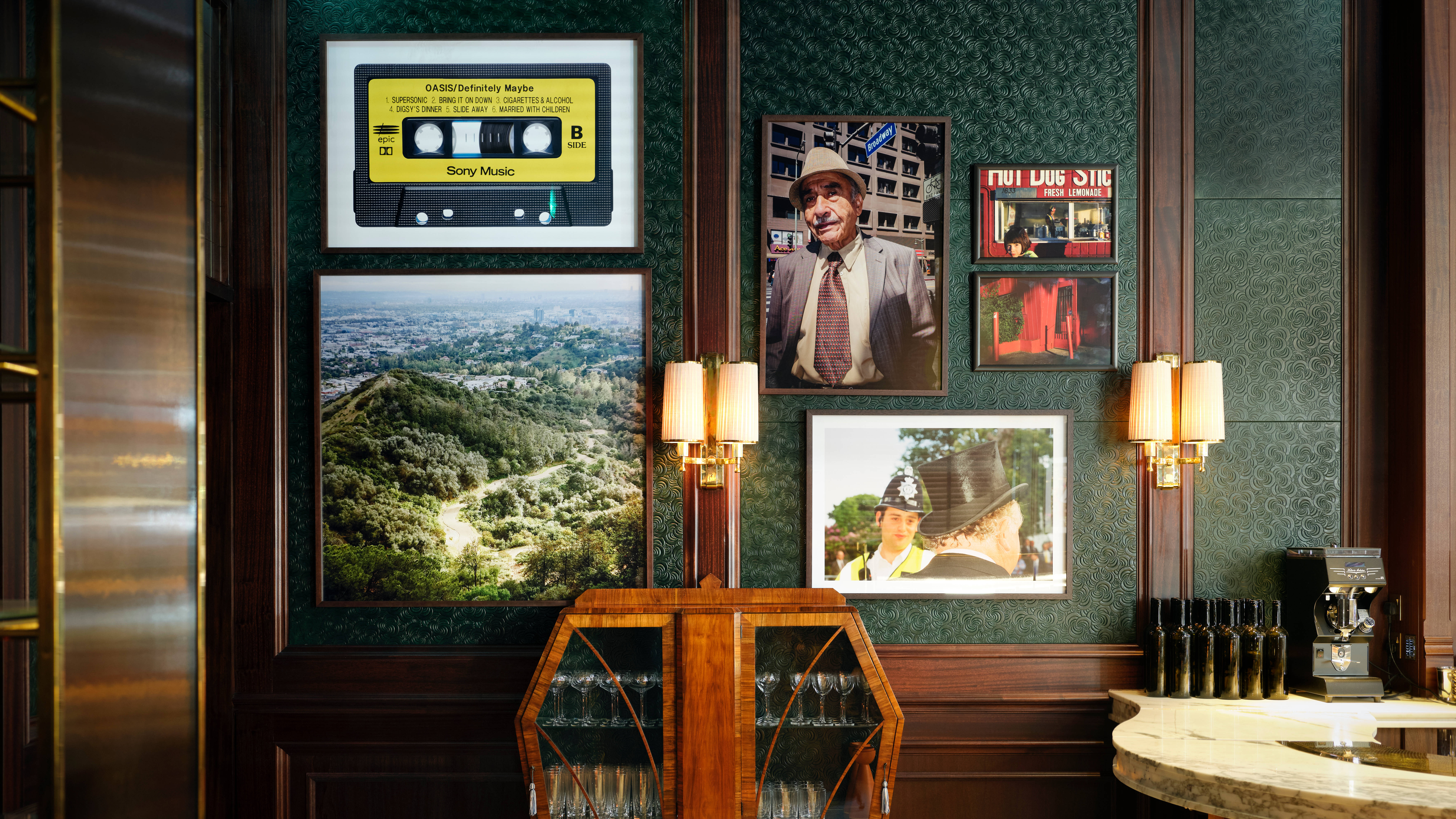 Side Hustle bar with dark green walls, a wooden wine cabinet, framed vintage photos and a yellow cassette tape on the wall.