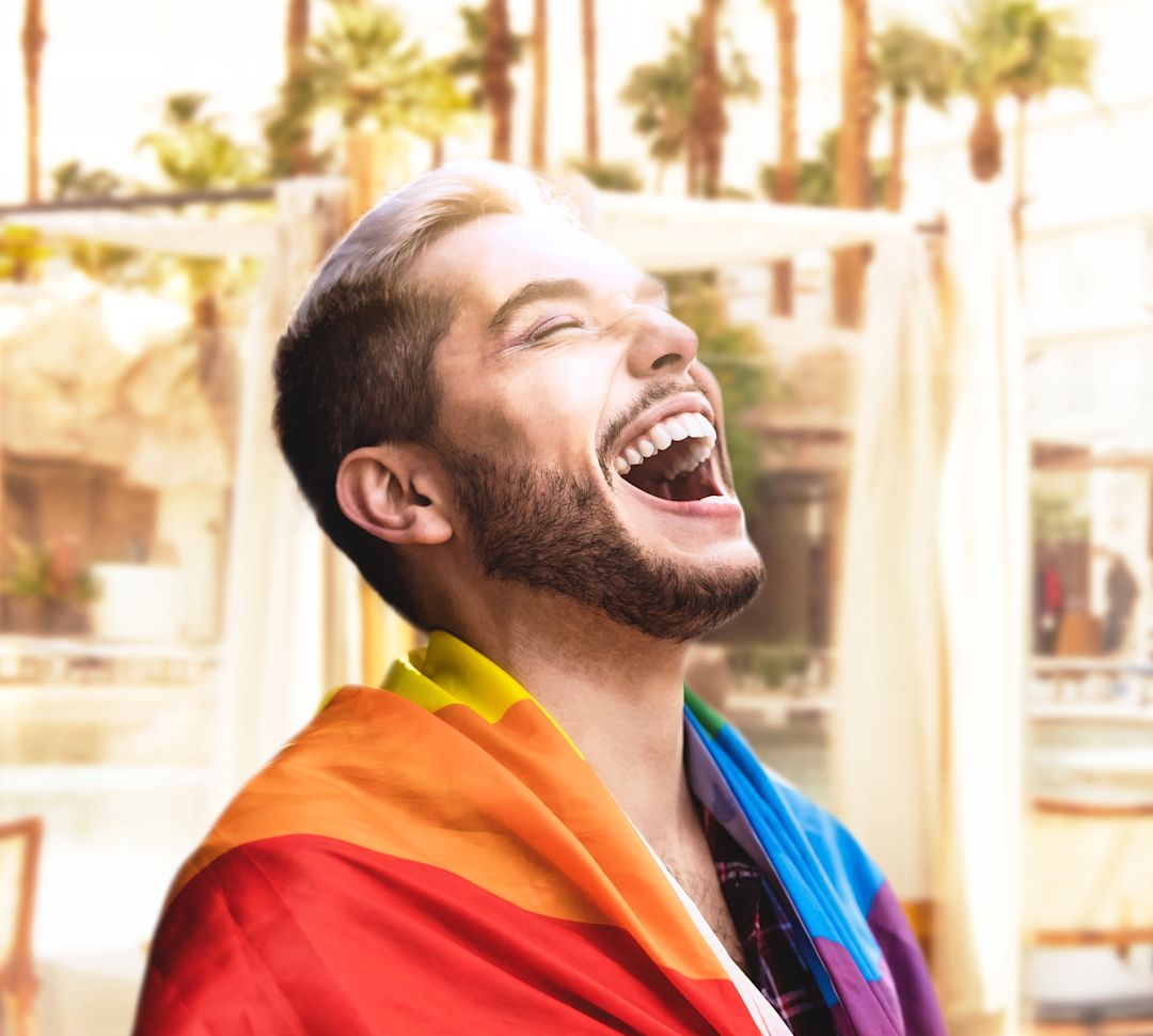 Man laughing with rainbow flag draped around shoulders