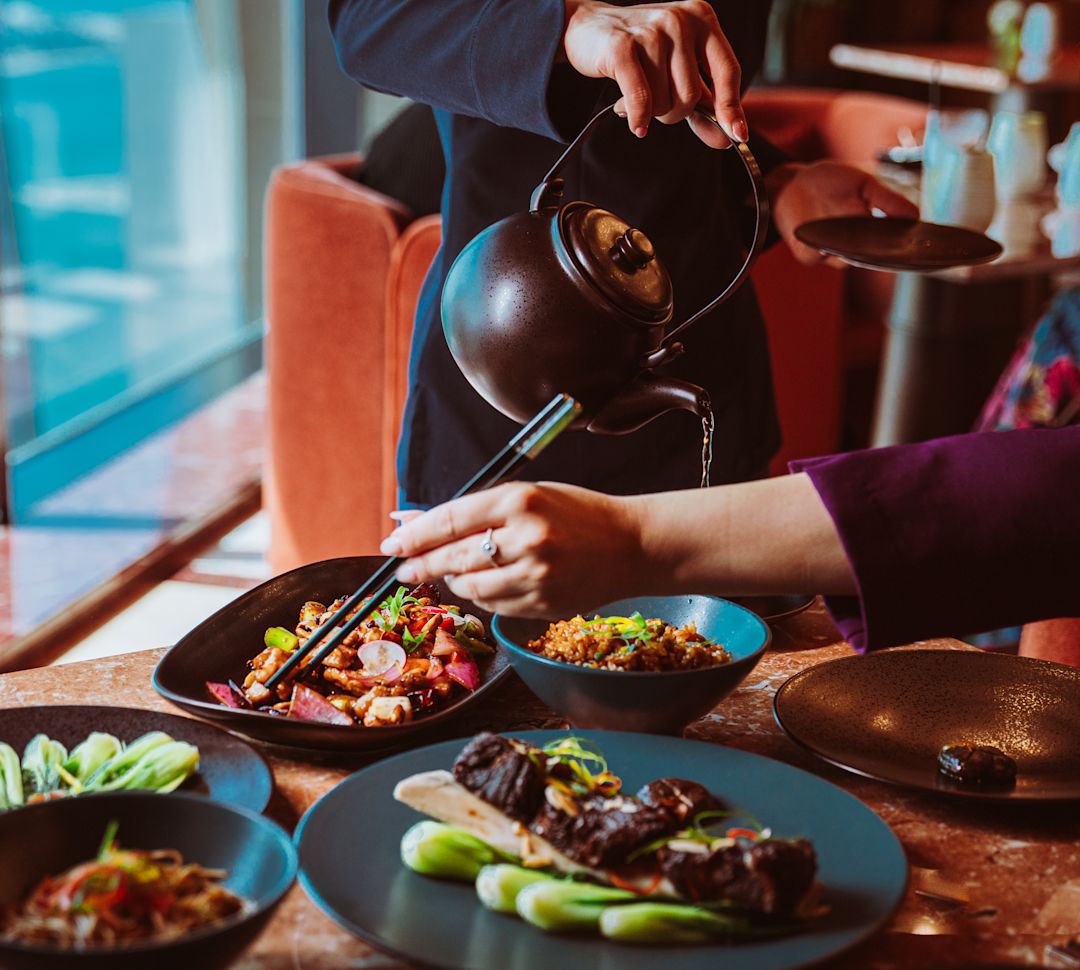 Person Serving Tea and Another Dining at Yun Restaurant