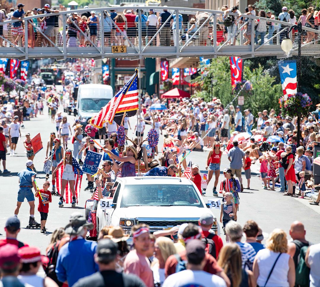 People in downtown along the street watching the July 4th parade.