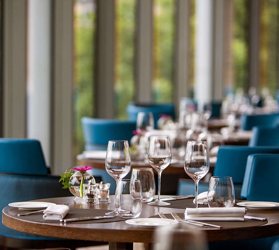 Wooden table set with glassware and cutlery with blue chairs.
