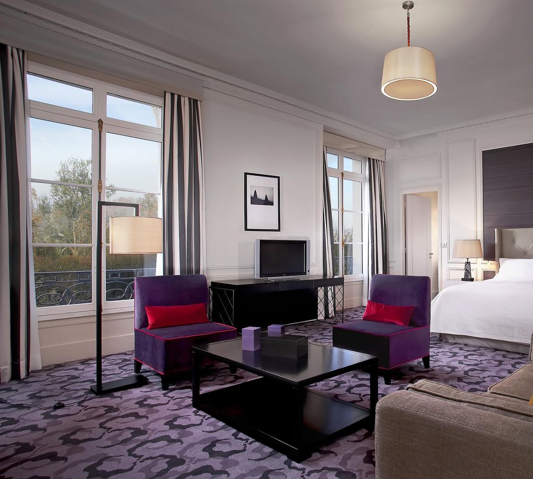 Blick auf das Bett der Junior Suite mit Kingsize-Bett und den Loungebereich mit großen Fenstern