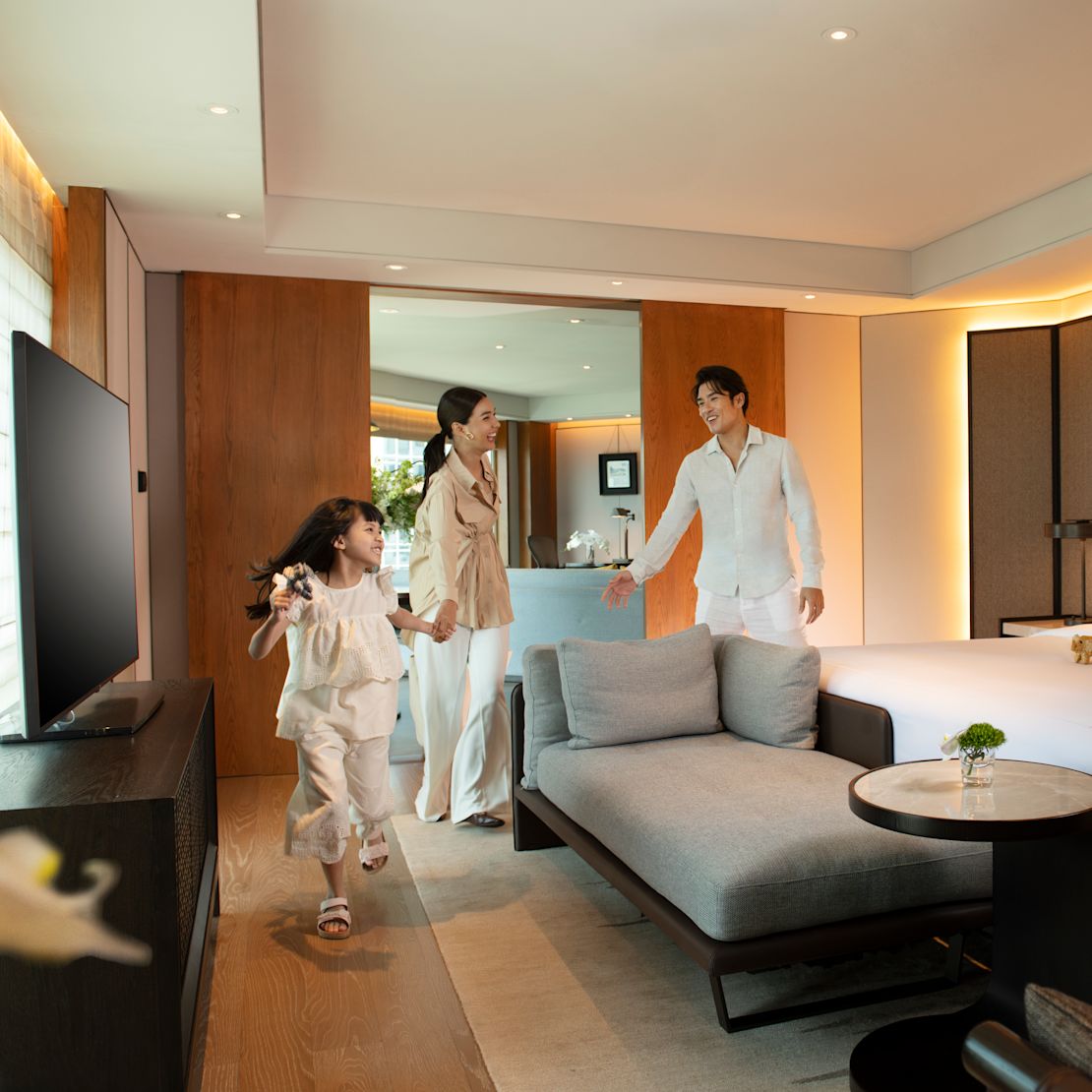 A couple with a little girl standing next to the king bed in the family suite bedroom.-transition