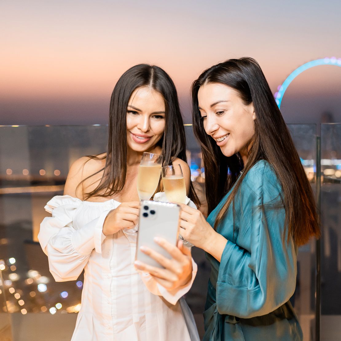 Two girls looking at their phone with the Dubai Eye at night behind them