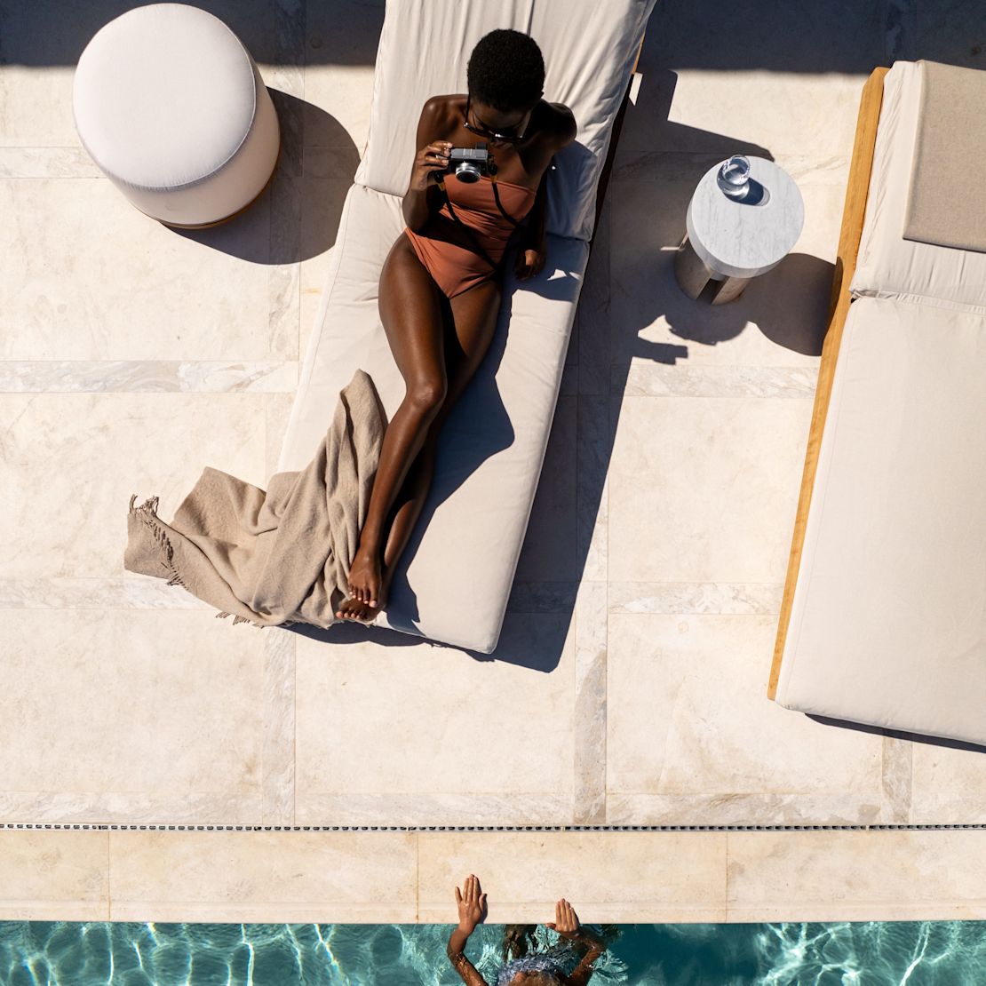 Foto in alto di una donna distesa sul lettino che scatta una fotografia con una piscina