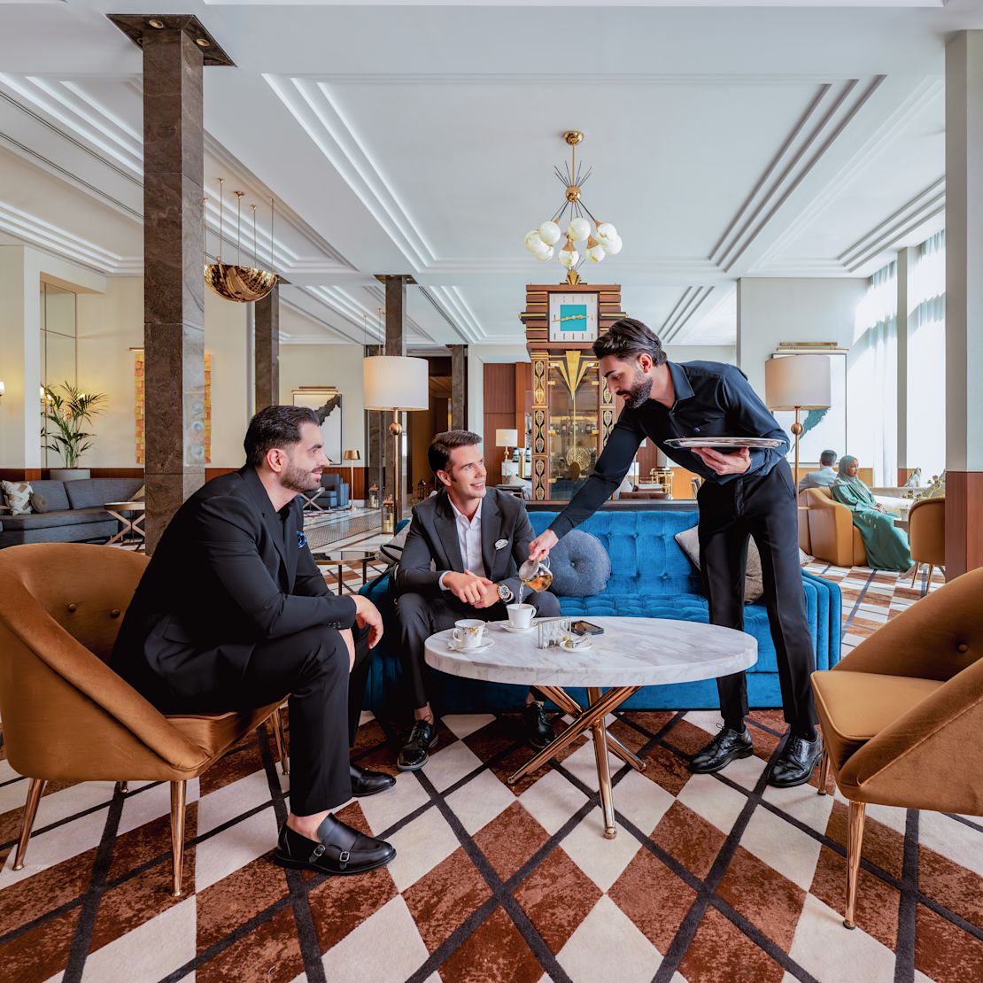Two men sitting in lobby area as staff member serves-transition