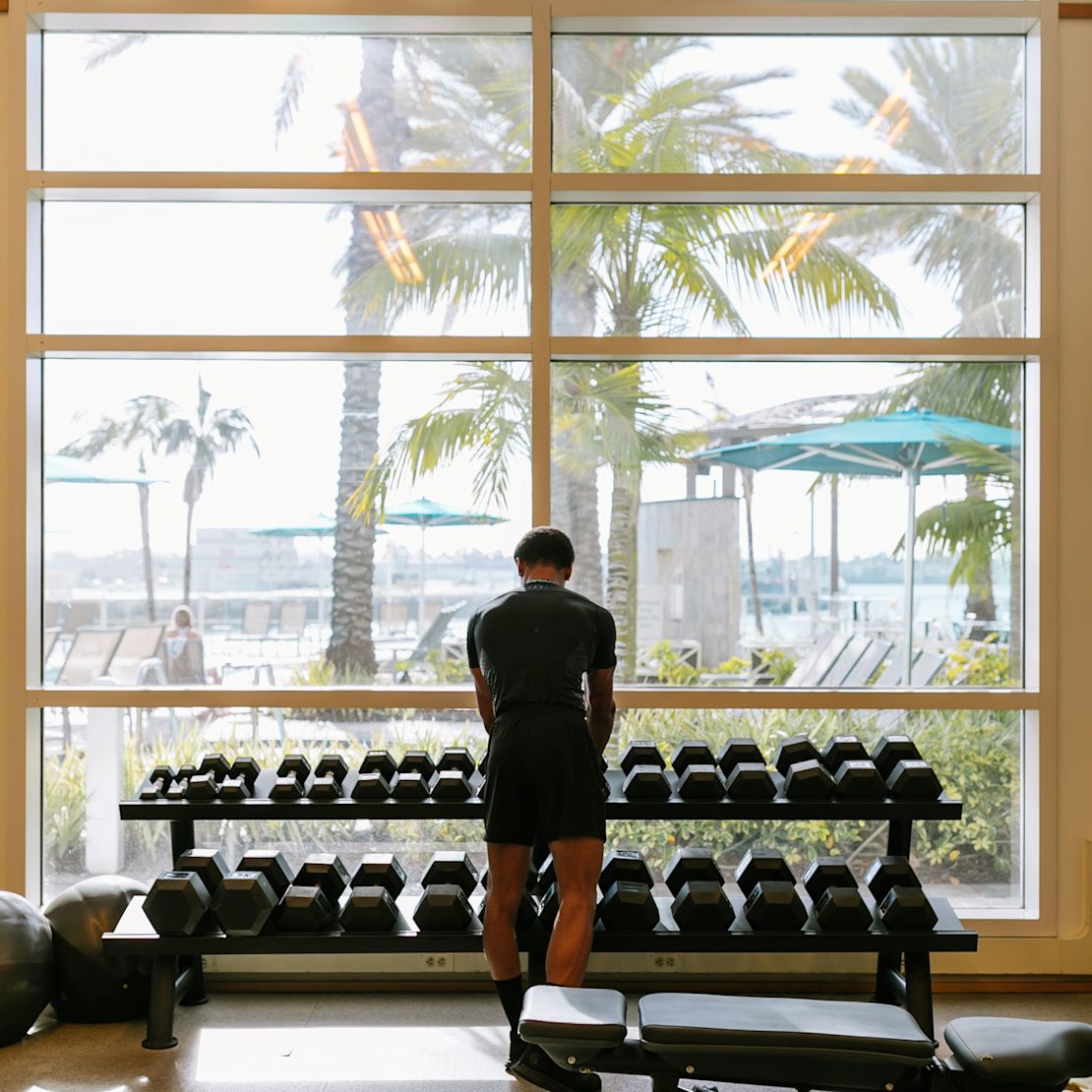 Un hombre comprobando las pesas en un gimnasio con ventanas grandes en transición