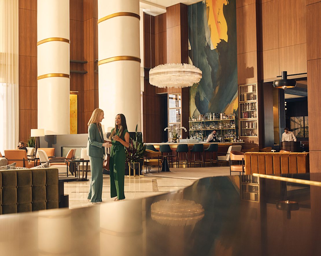 Two women standing in spacious lobby area with bartender behind-transition