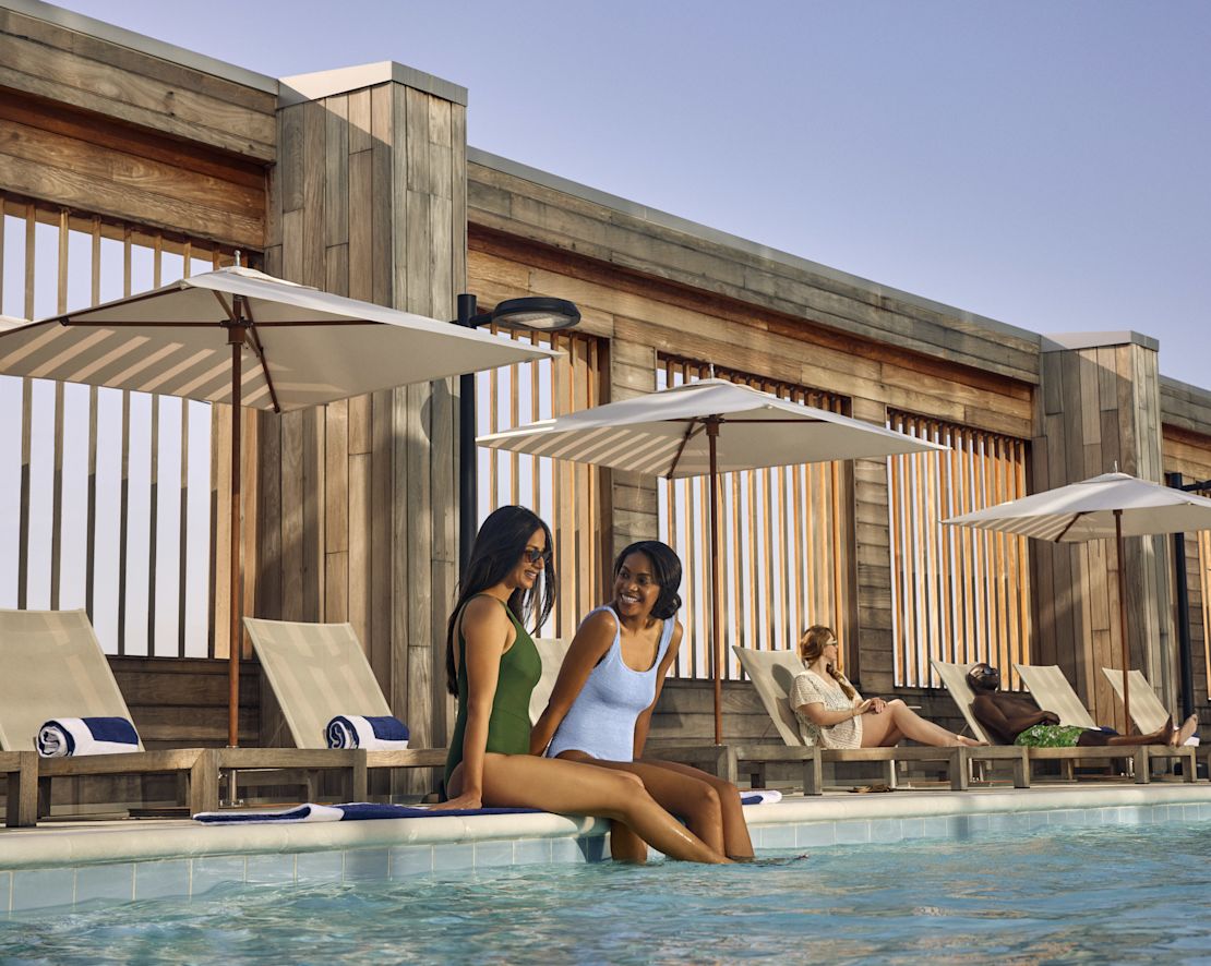 Two woman relaxing by the side of the pool, with legs in the water-transition