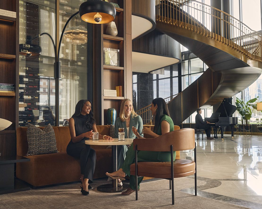 Group of 3 women sitting in lobby area with drinks-transition