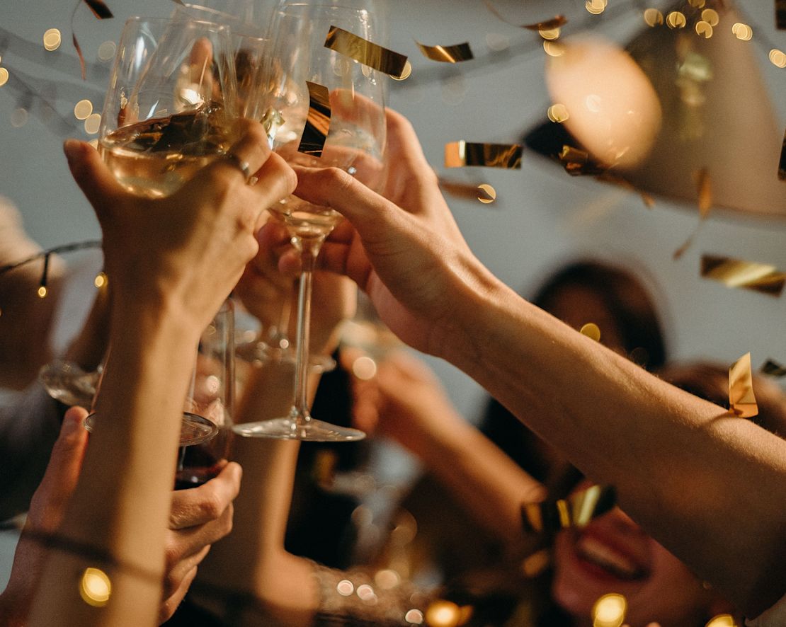 Gruppo di persone che festeggiano e alzano i bicchieri in una fase di transizione precedente al brindisi