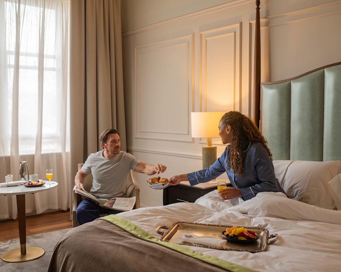 Woman sitting on bed handing over a bowl of pastries to man-transition
