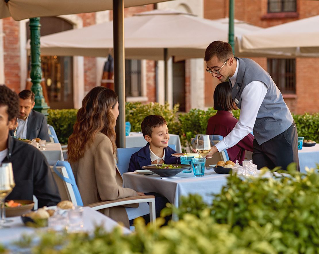 Waiter serving mother and sun lunch on the restaurant terrace-transition