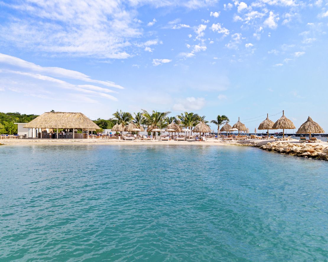 Außenansicht mit Blick auf einen Strand und Lounge-Sessel unter den Sonnenschirmen – Übergang