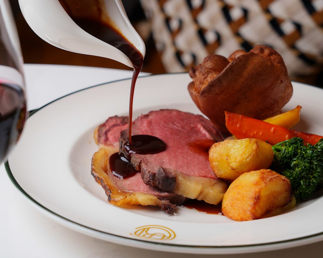 Person, die Sauce auf einem Teller mit Fleisch und Kartoffeln im "Court"-Übergang zaubert