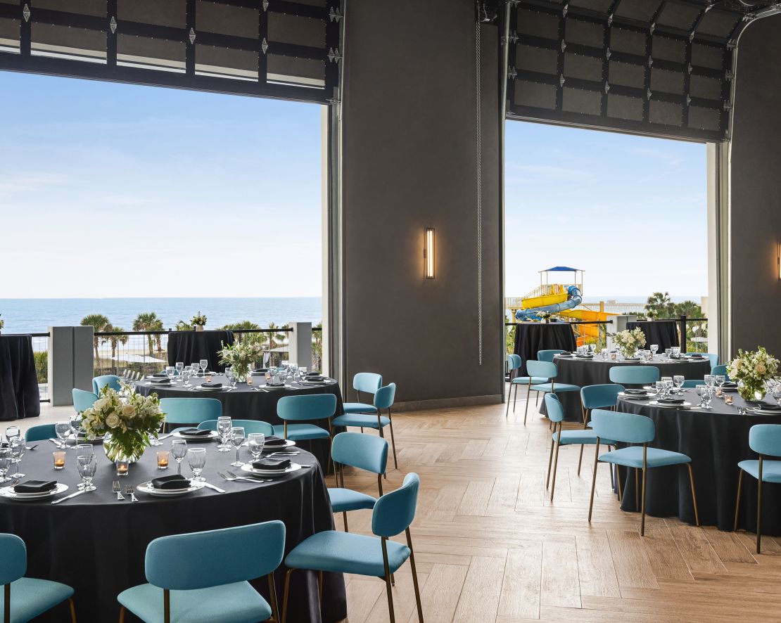 Beautiful on-site ballroom featuring banquet setup with large roll up doors open to terrace and ocean view-transition