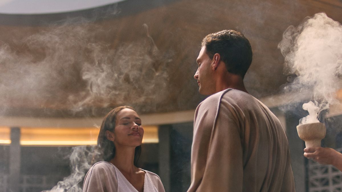 A woman and a man are holding hands while standing in the spa and  team members are holding bowls with smoking incense