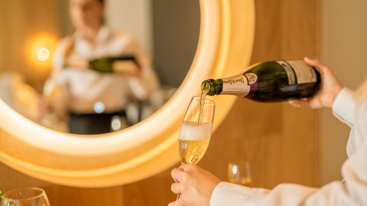 Frau schenkt Champagner in einem Glas in einem Hotelzimmer