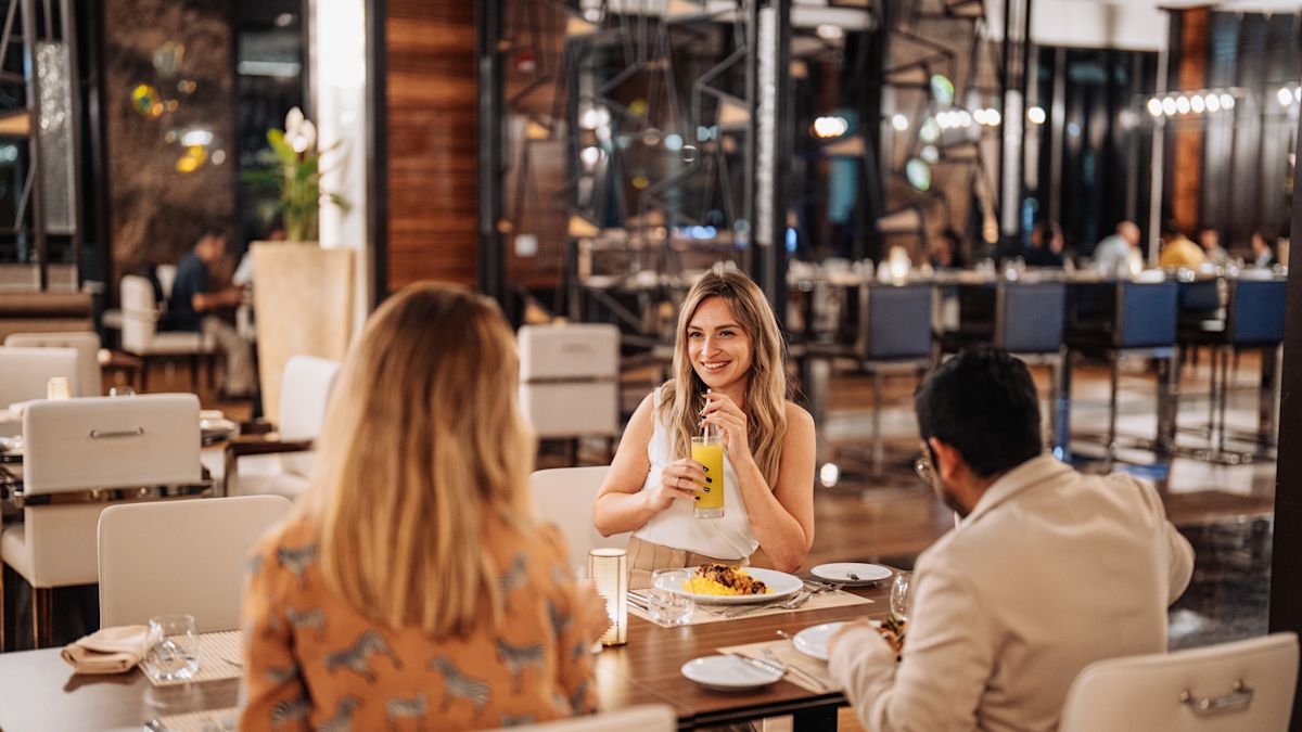 3 people sitting at table, with woman drinking from glass
