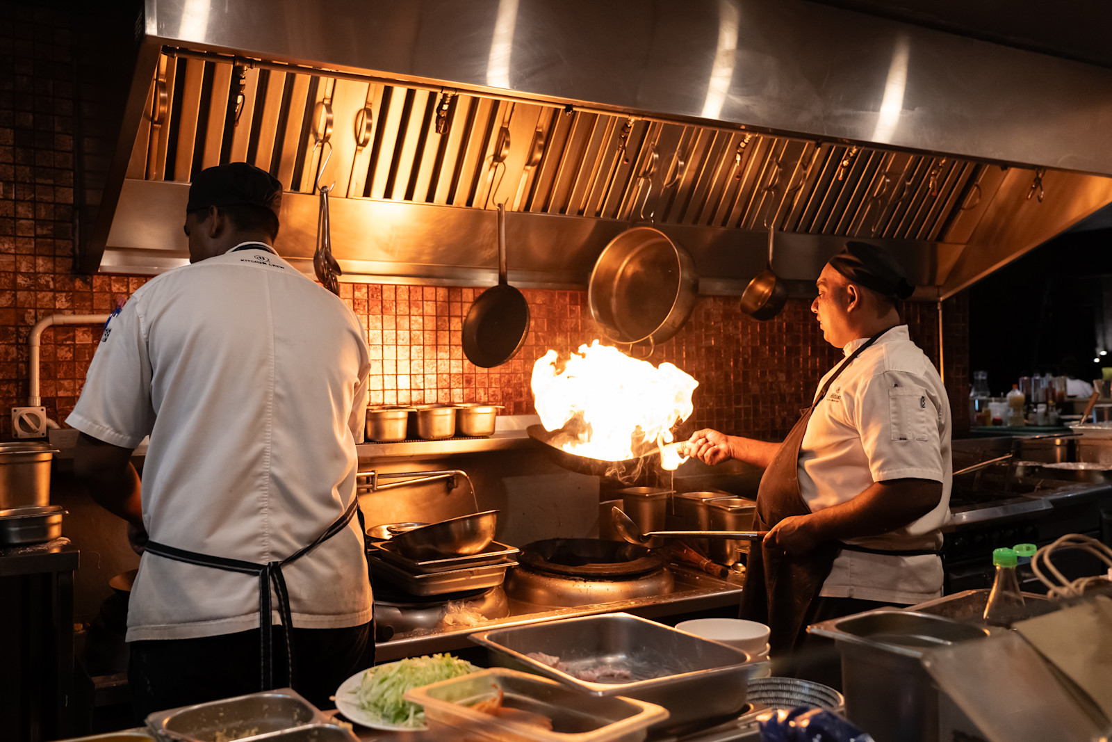 Two chefs at work in the kitchen, with flaming pan