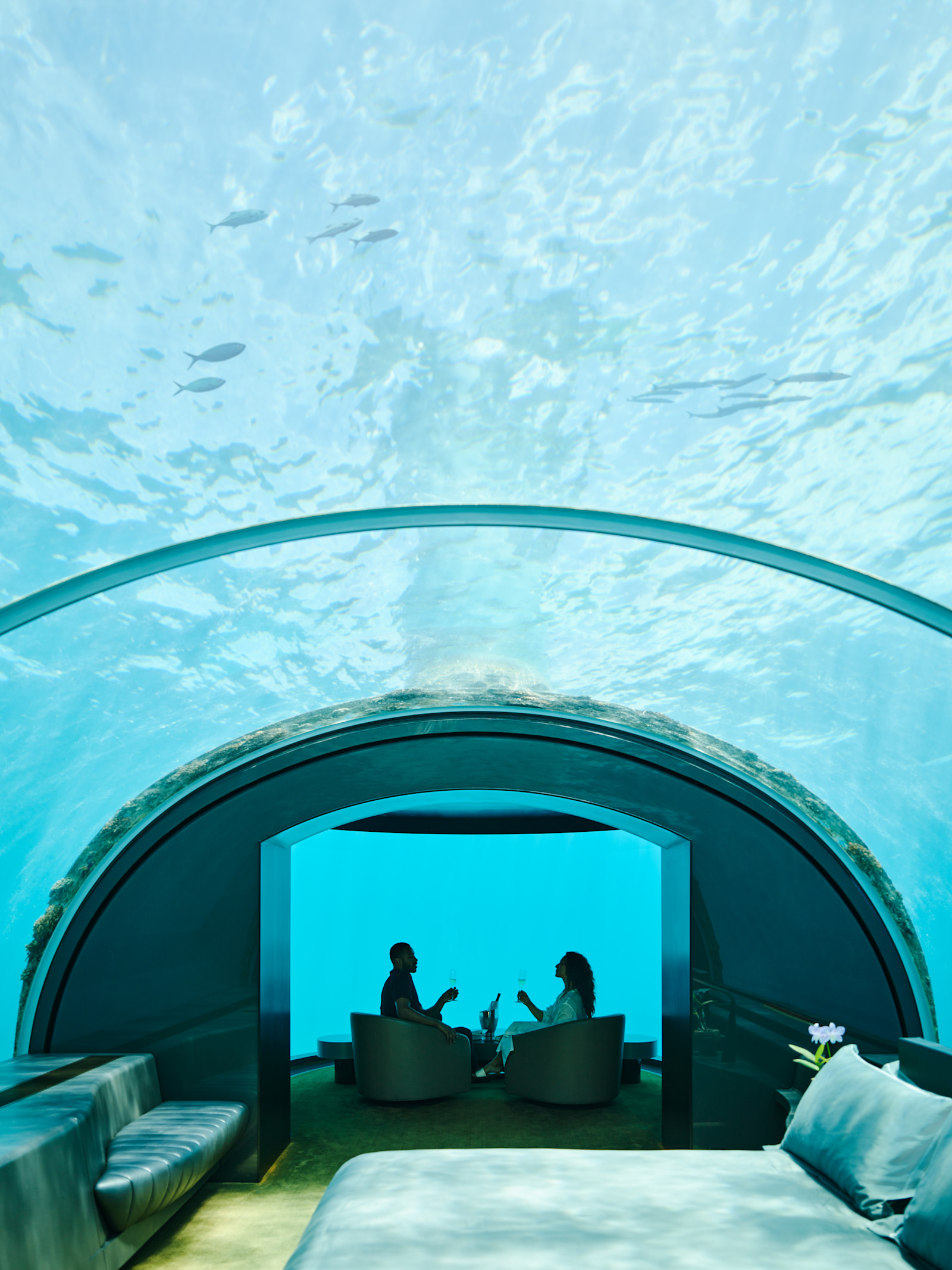 Chambre sous-marine, avec un homme et une femme se relaxant sur des chaises tandis que des poissons nagent au-dessus de leur tête
