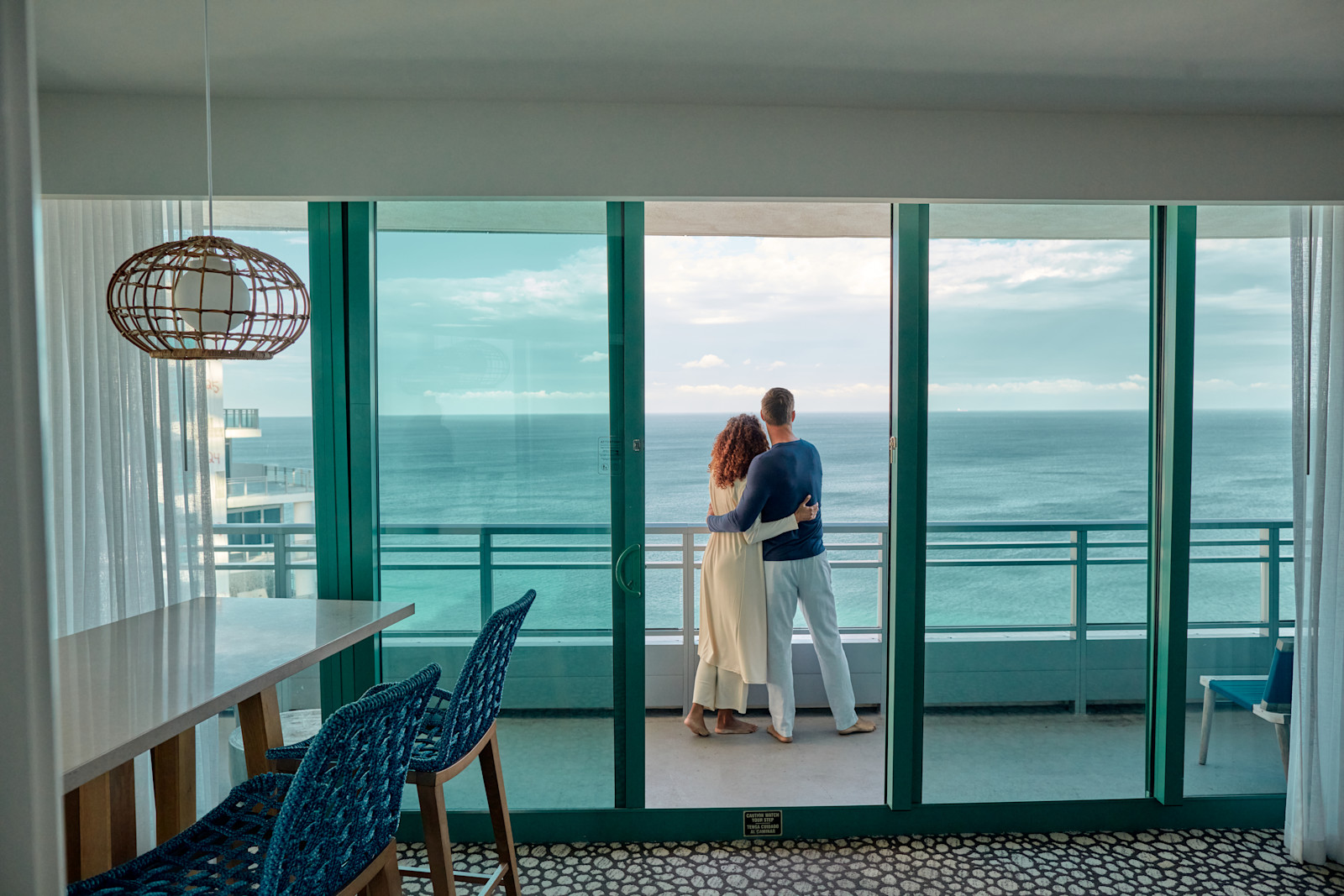 Bărbat și femeie îmbrățișându-se în timp ce stau la balconul exterior cu vedere spre ocean