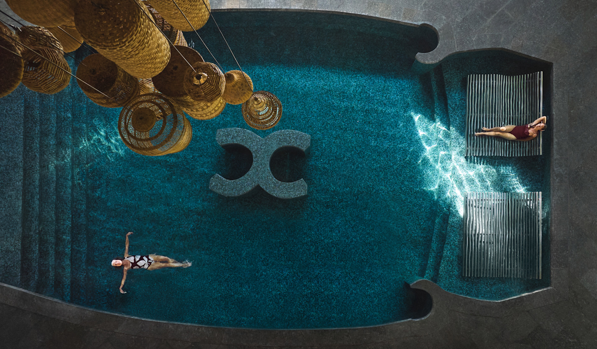 Vedere de tip „ochi de păsări” a unei femei care plutește pe spatele ei în piscină, relaxându-se în timp ce o altă femeie stă într-unul dintre șezlongurile din piscină