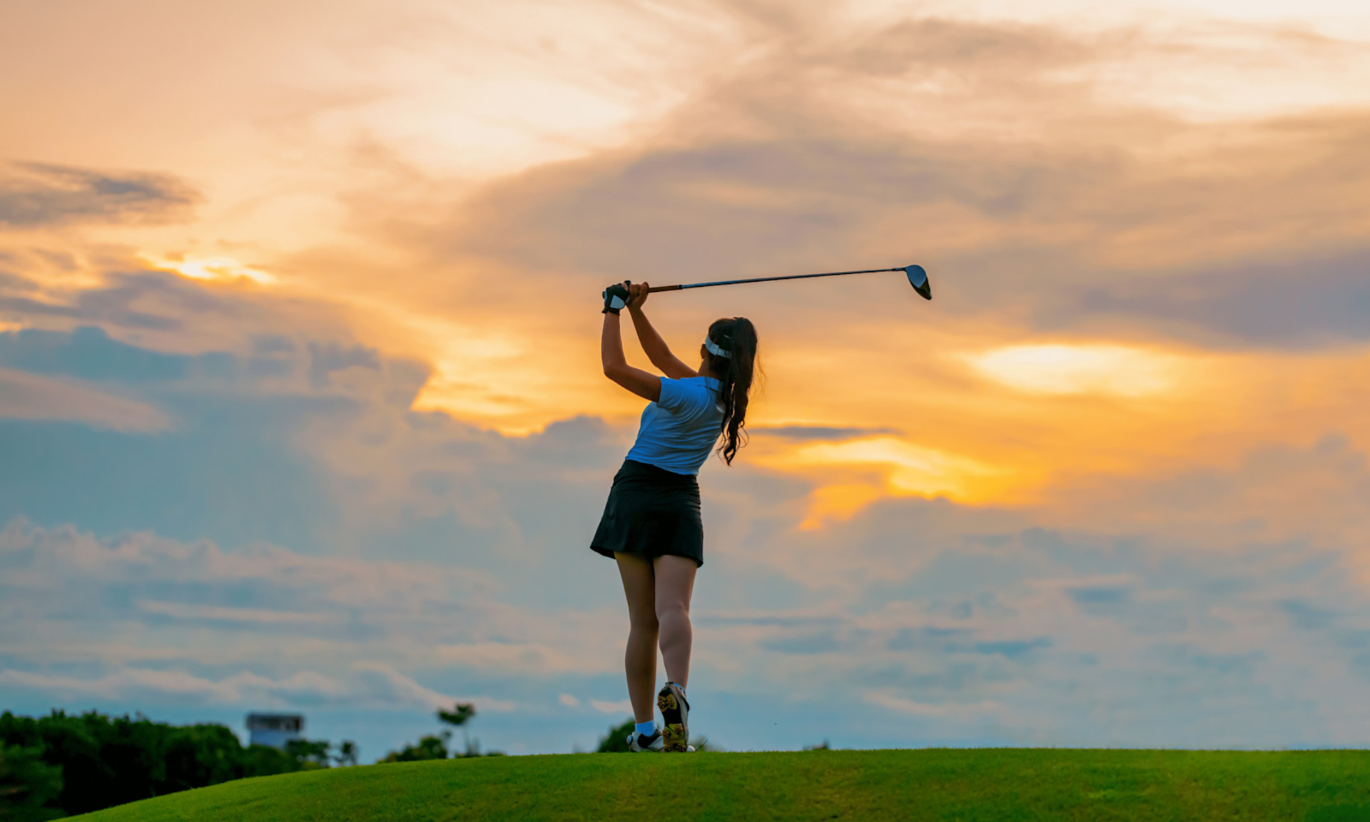 Woman standing on golf course with club held aloft after completing swing