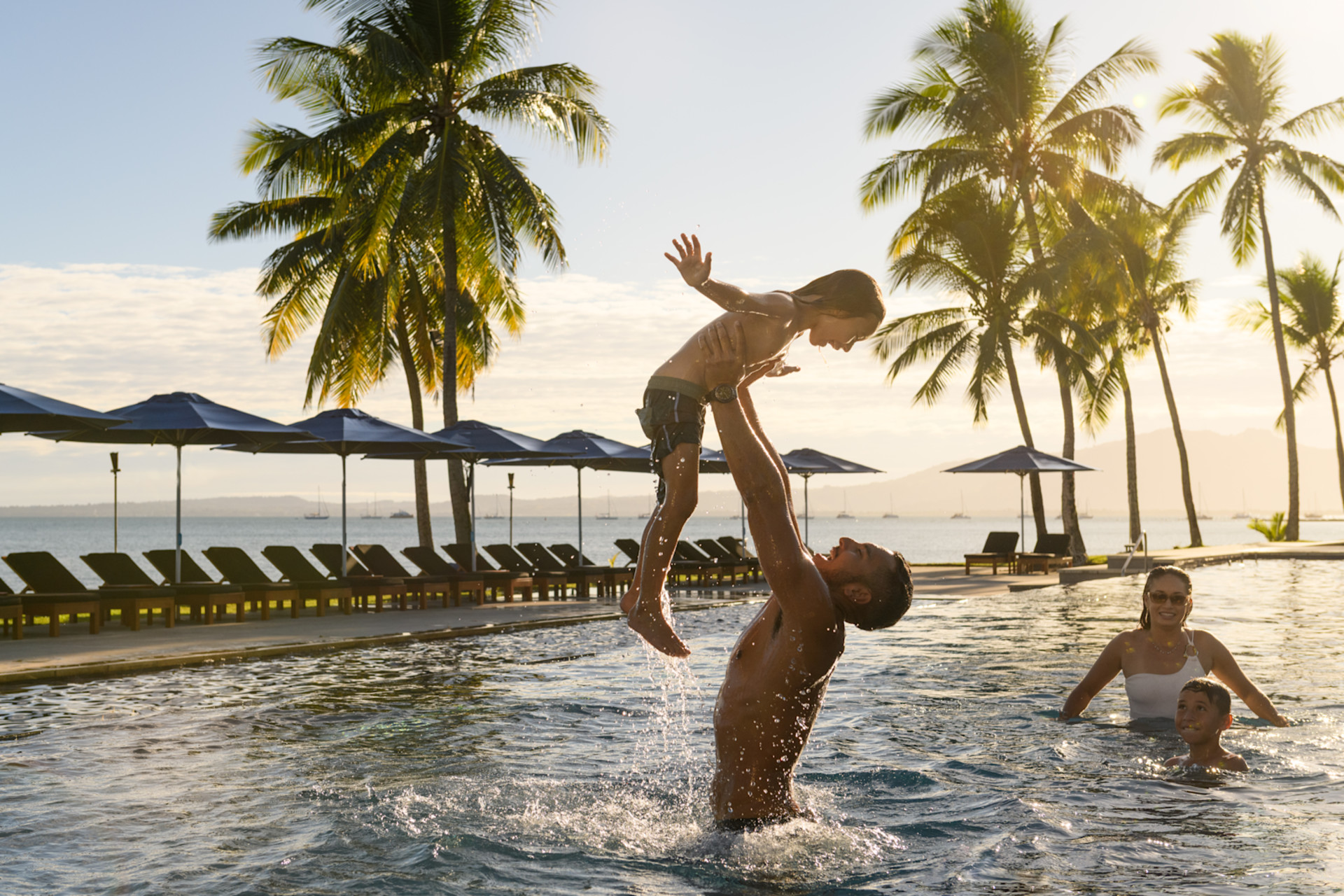 Uomo che solleva il bambino dall'acqua con una donna e un bambino dietro la piscina
